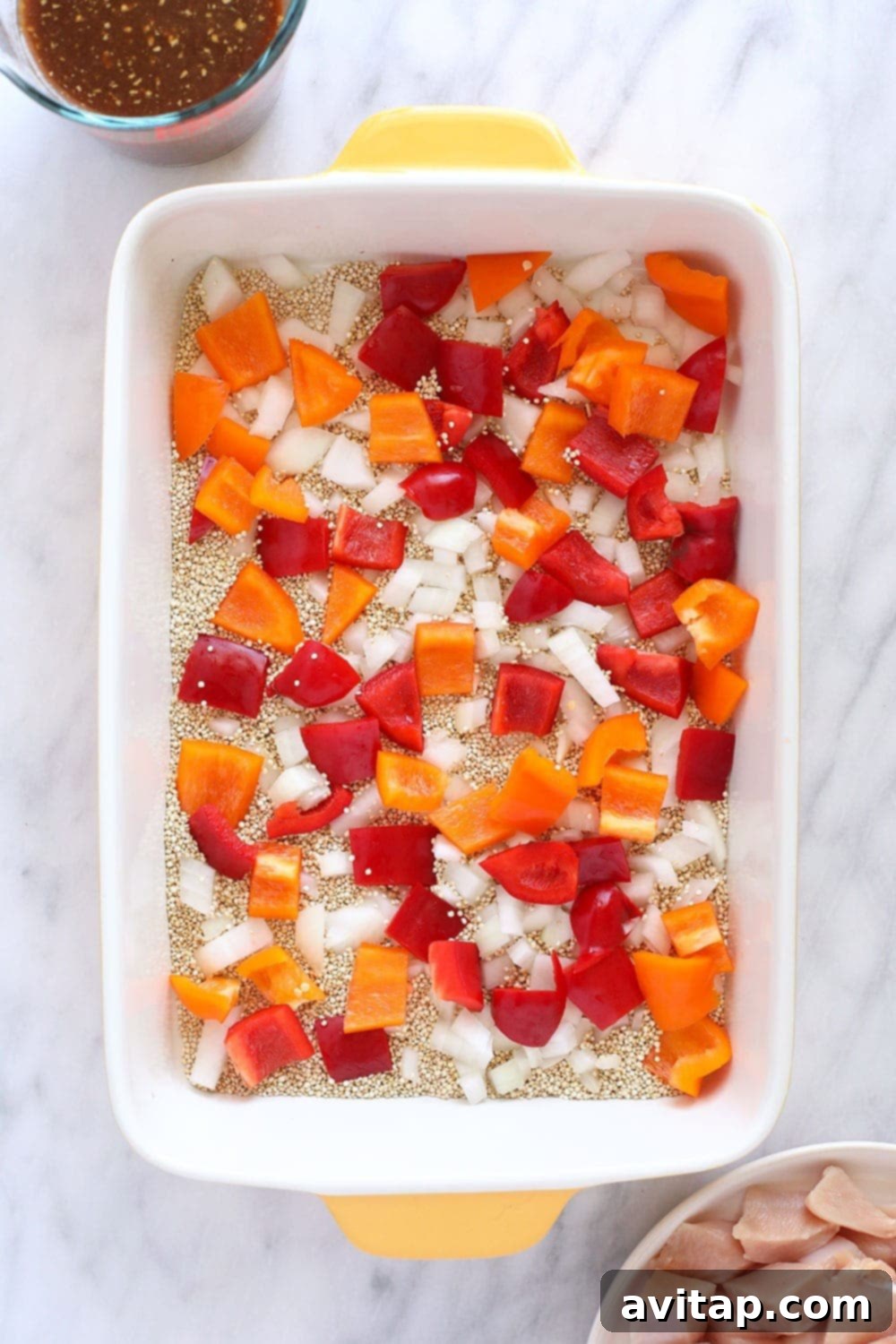 Wholesome Cashew Chicken Bake 3 Uncooked quinoa, vibrant bell peppers, and minced onion layered in a casserole dish, ready for the oven.