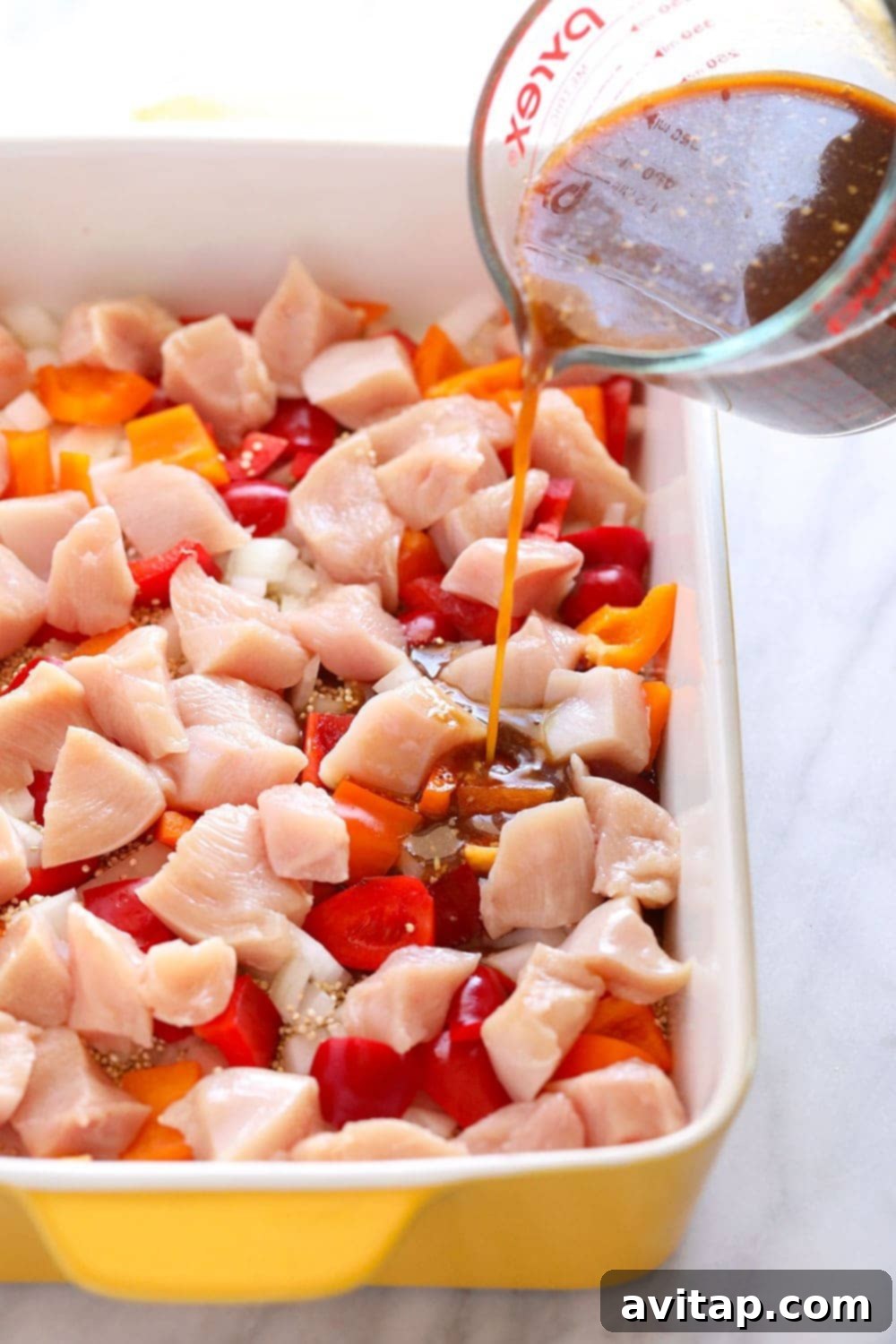Wholesome Cashew Chicken Bake 4 Savory cashew chicken sauce being poured over layered chicken and vegetables in a casserole dish.