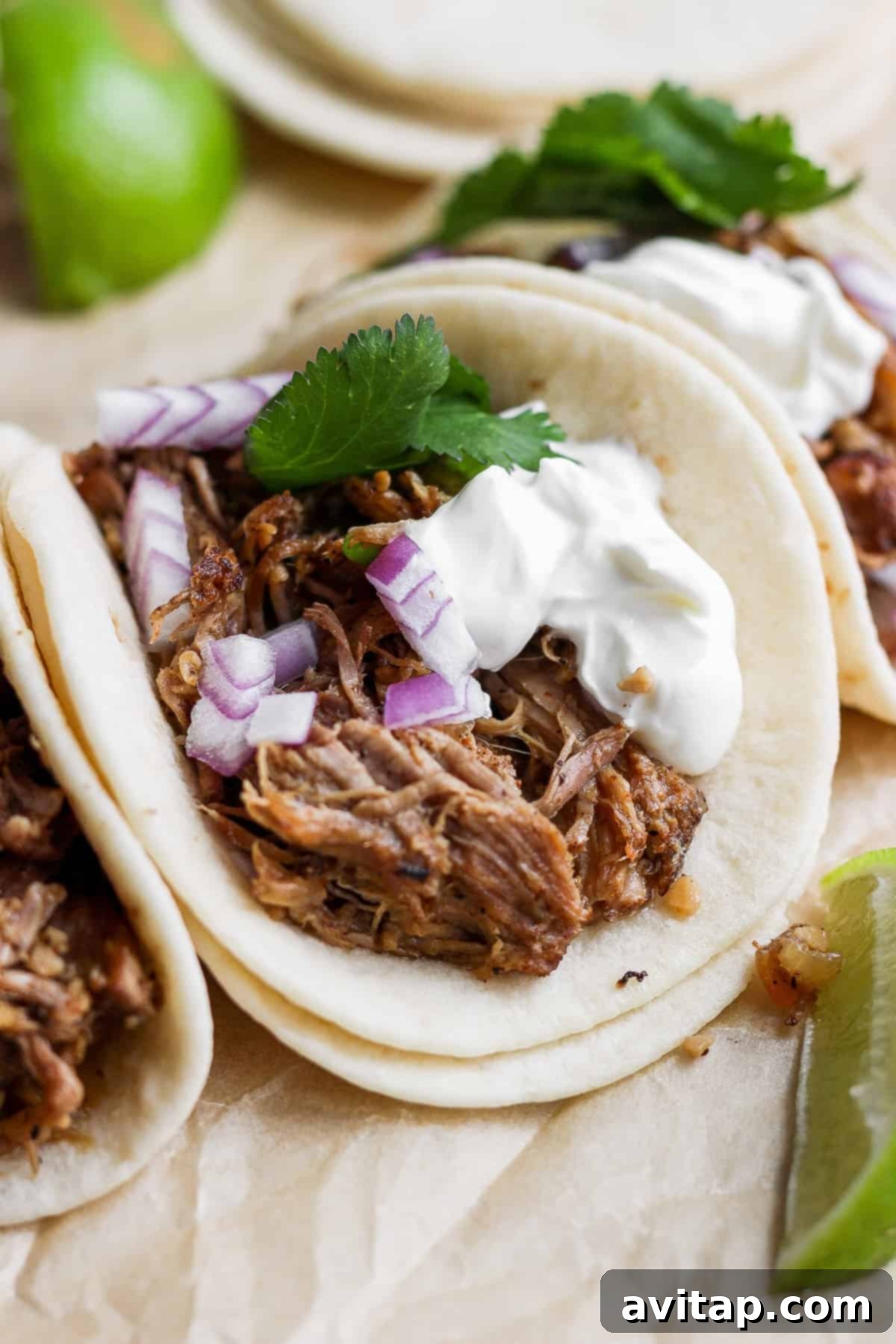 Close-up of a plate of assembled carnitas tacos, garnished with red onion, Greek yogurt, and cilantro.