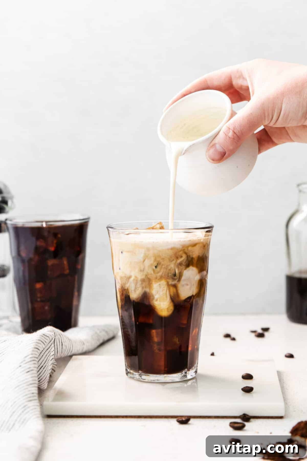Pouring cream into cold brew coffee, showcasing its rich, dark color and refreshing appeal.