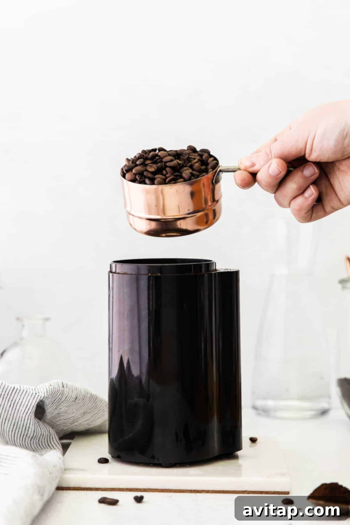 Pouring coffee beans into a coffee grinder, highlighting the initial step of fresh preparation.