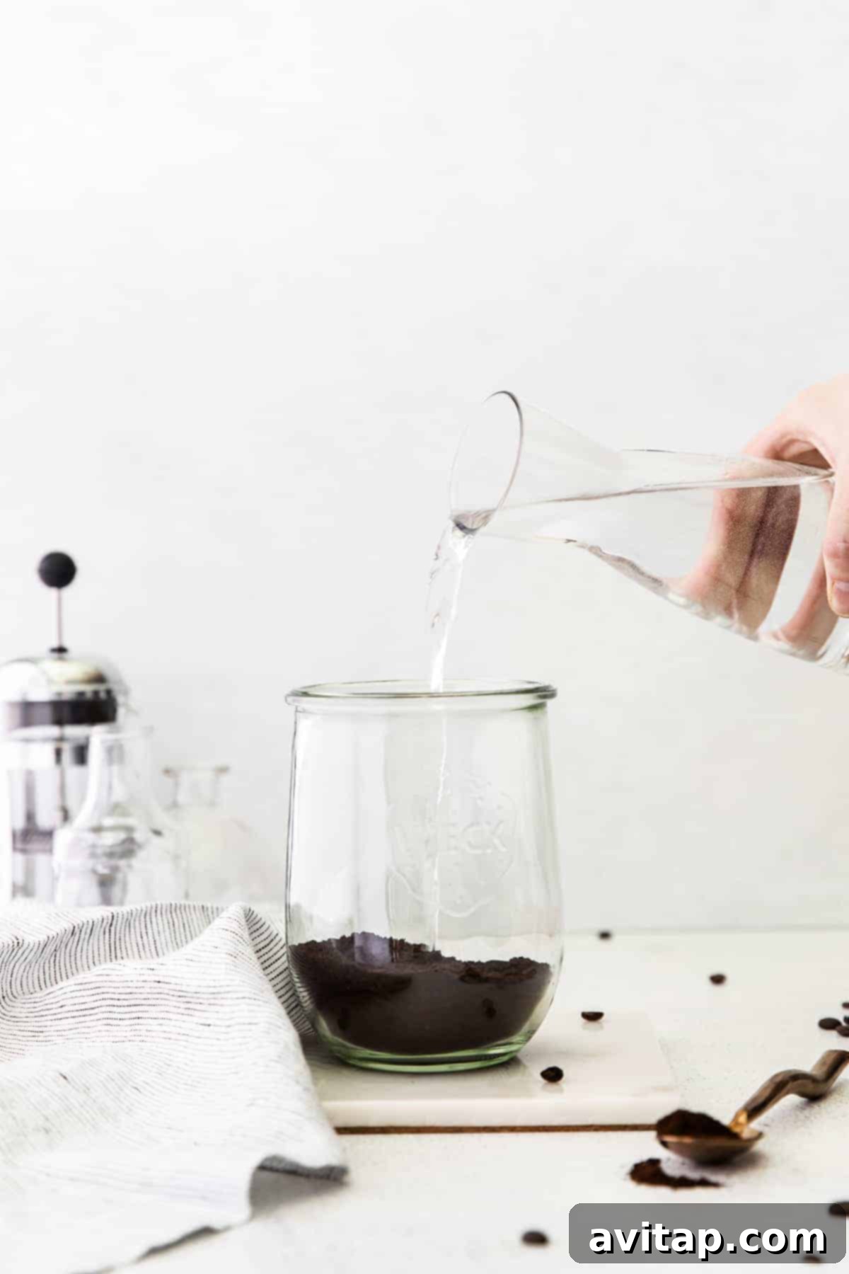 Pouring water over coffee grounds in a jar to initiate the cold brewing process.