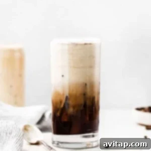 A close-up of an iced latte in a clear glass, showing the creamy layers of cold brew and vanilla sweet cream, ready to drink.