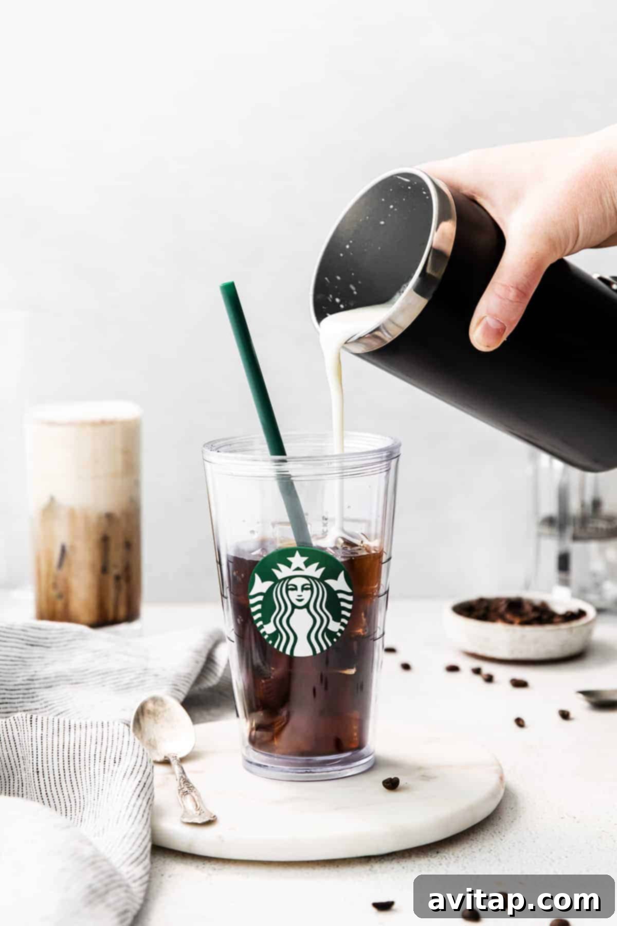 Velvet Vanilla Cold Brew 13 A hand gently pouring a stream of vanilla sweet cream into a glass filled with cold brew and ice, creating a beautiful and appetizing swirl pattern.