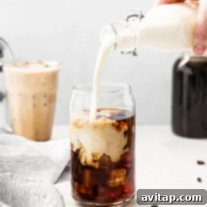 A person pouring vanilla sweet cream into a glass of iced cold brew coffee, demonstrating the assembly.