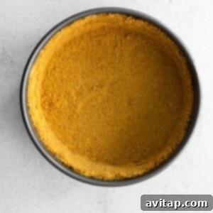 A yellow Greek yogurt cheesecake crust in a pan on a white background, pressed into a springform pan.