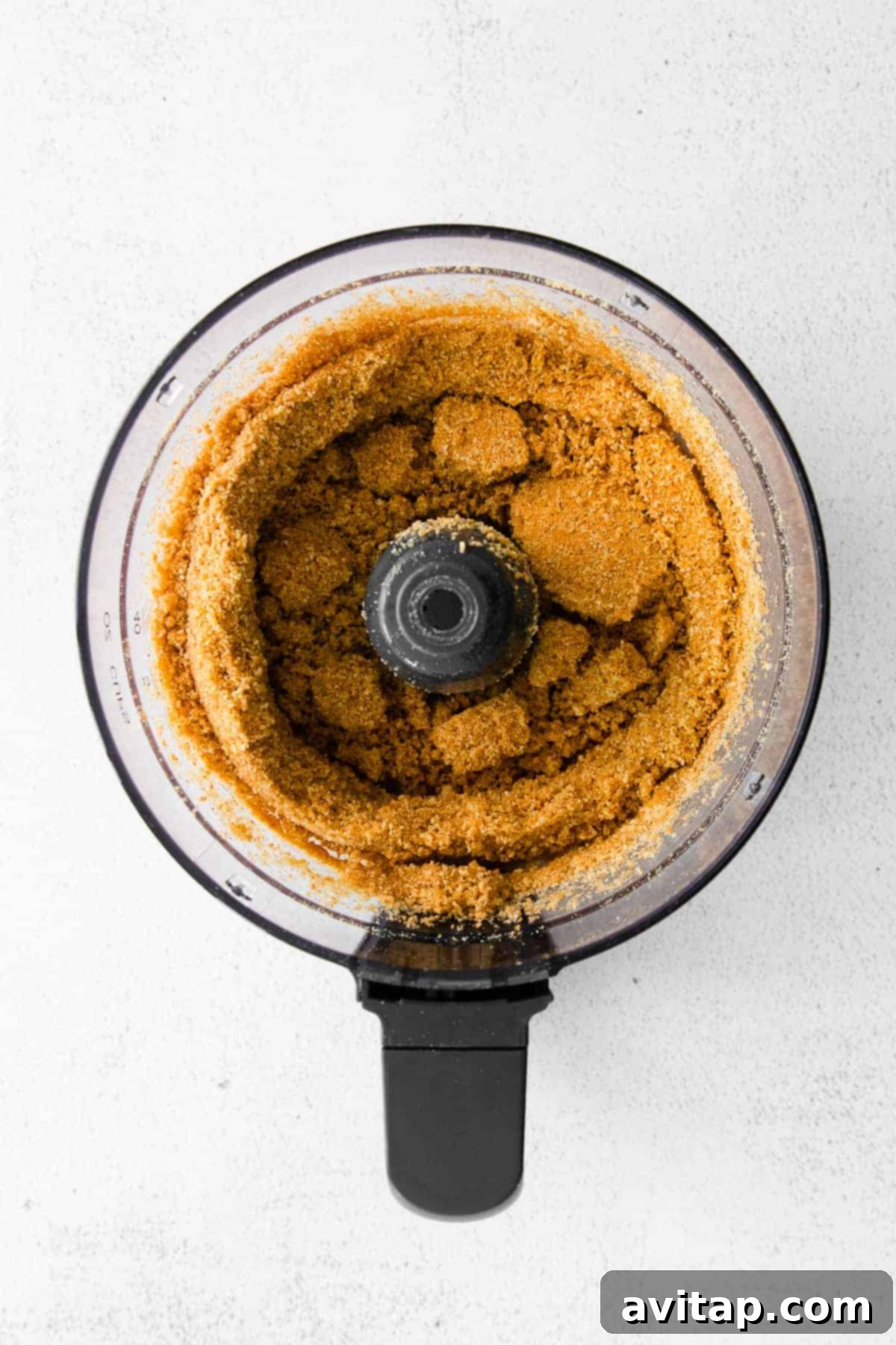 Graham cracker crumbs being expertly prepared in a food processor, a crucial first step for the cheesecake crust.