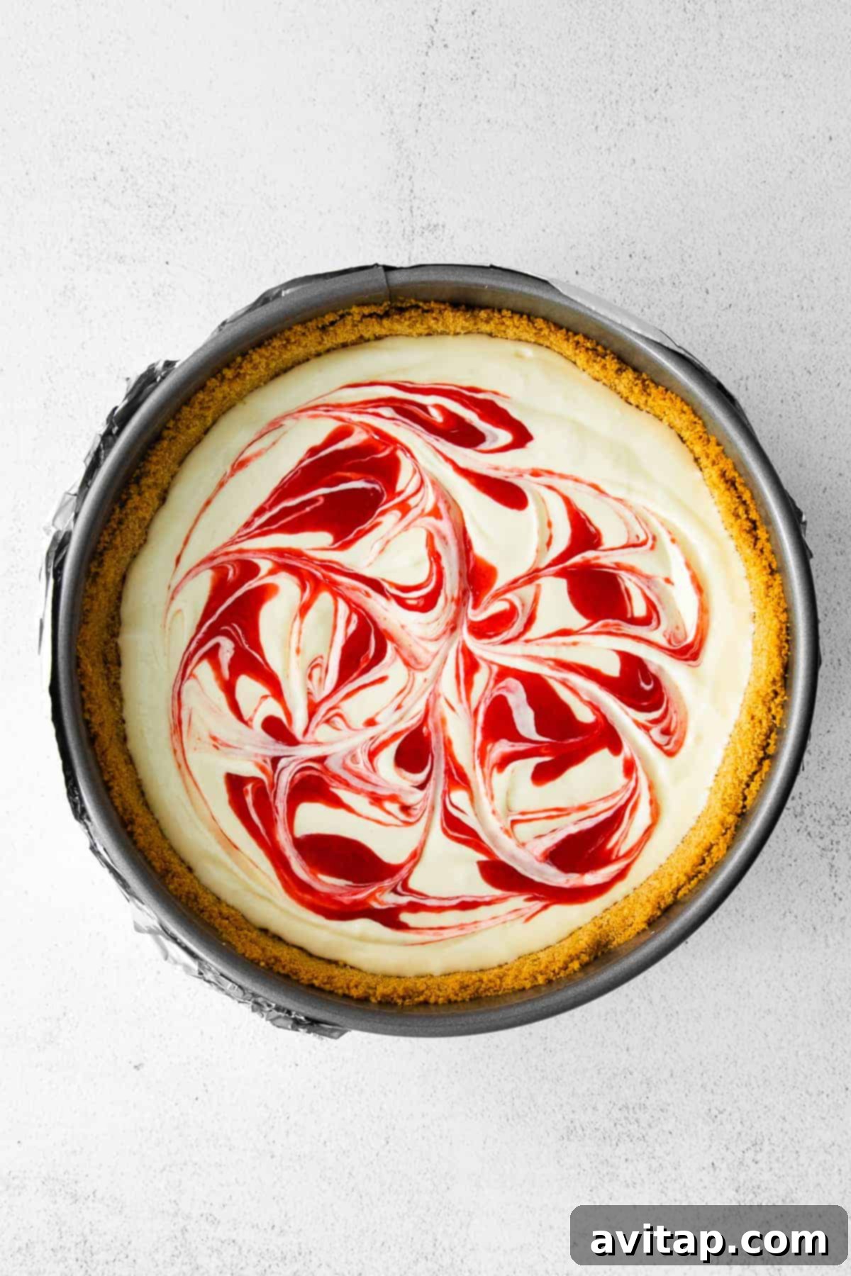 The Greek yogurt cheesecake filling, elegantly topped with a beautiful raspberry swirl, poised before baking.