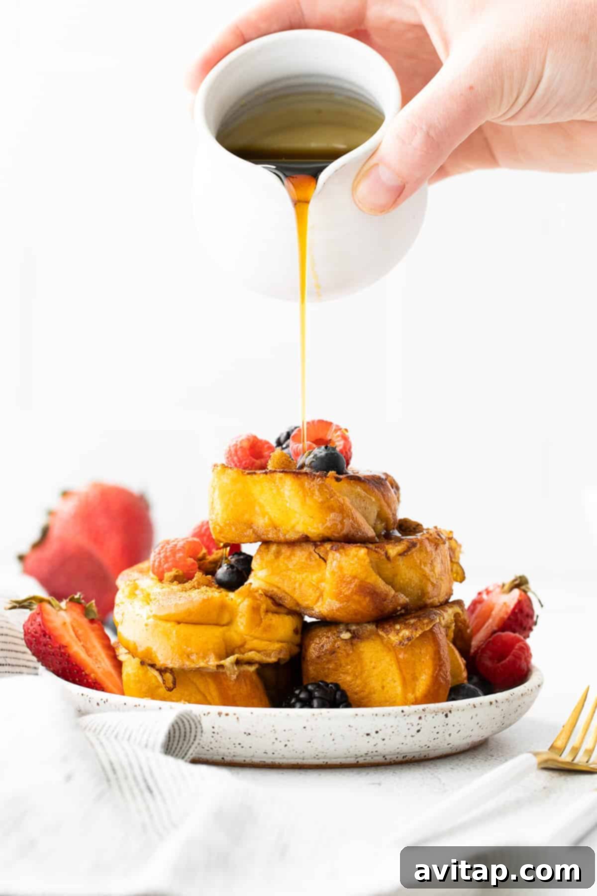 Golden French toast slices topped with fresh berries and maple syrup pouring over them.