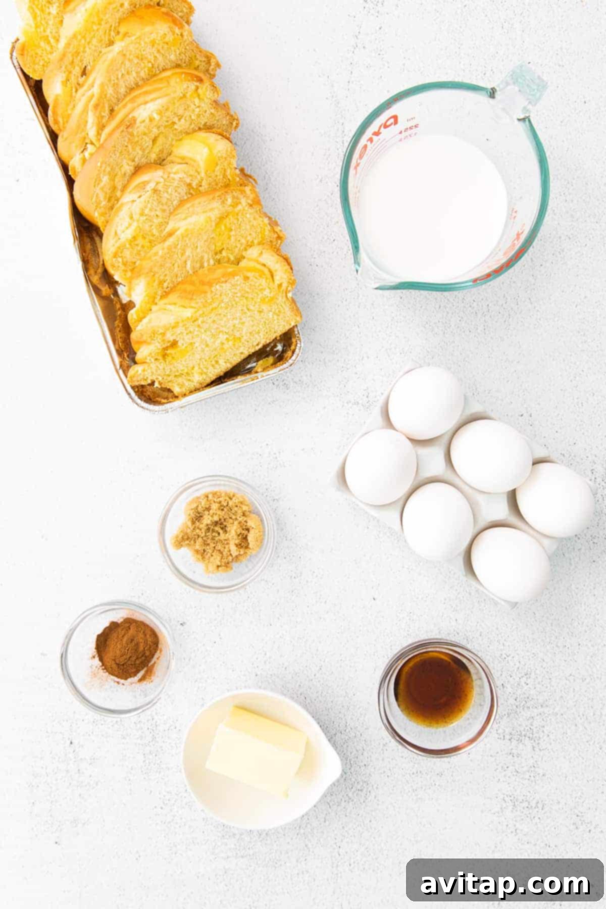 Key ingredients for French toast neatly arranged on a counter: eggs, milk, maple syrup, thick-cut bread, and butter.