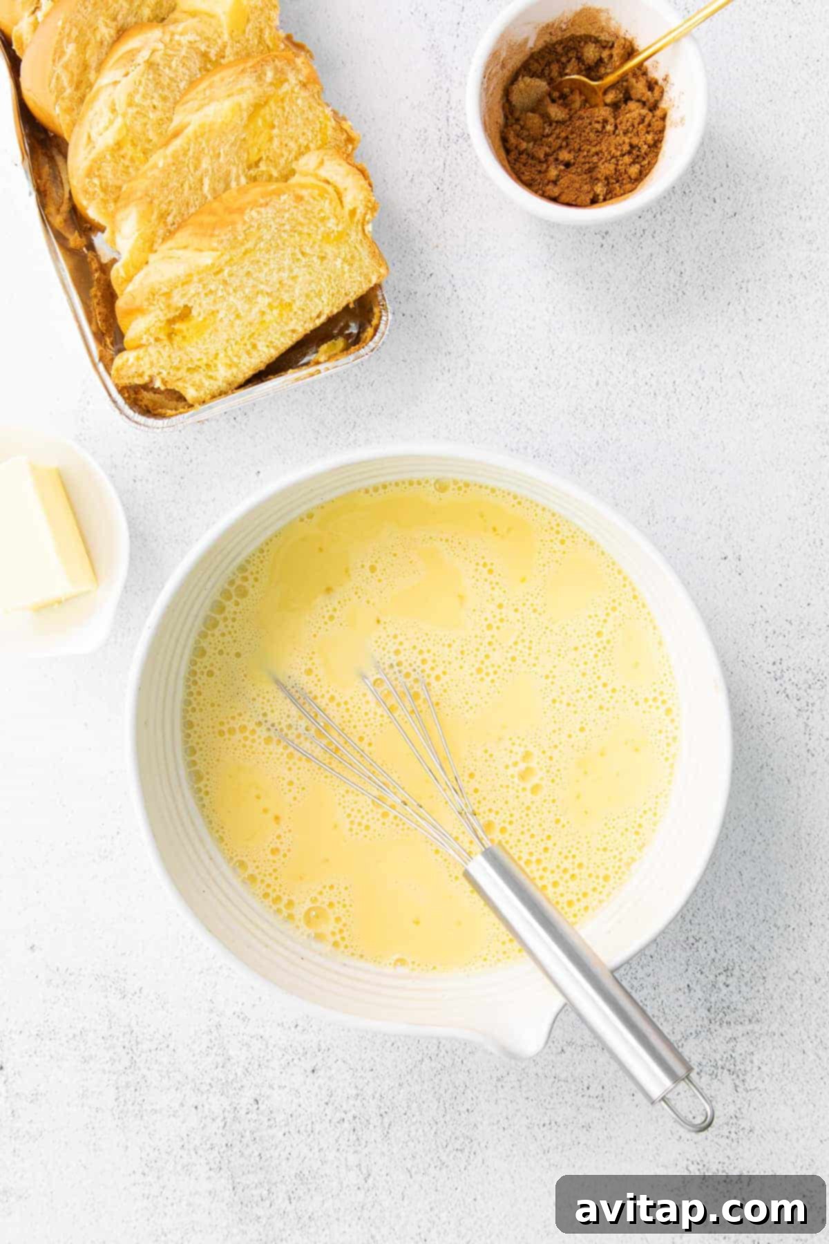 A bowl of egg wash mixture for French toast, with slices of thick-cut bread ready for dipping.