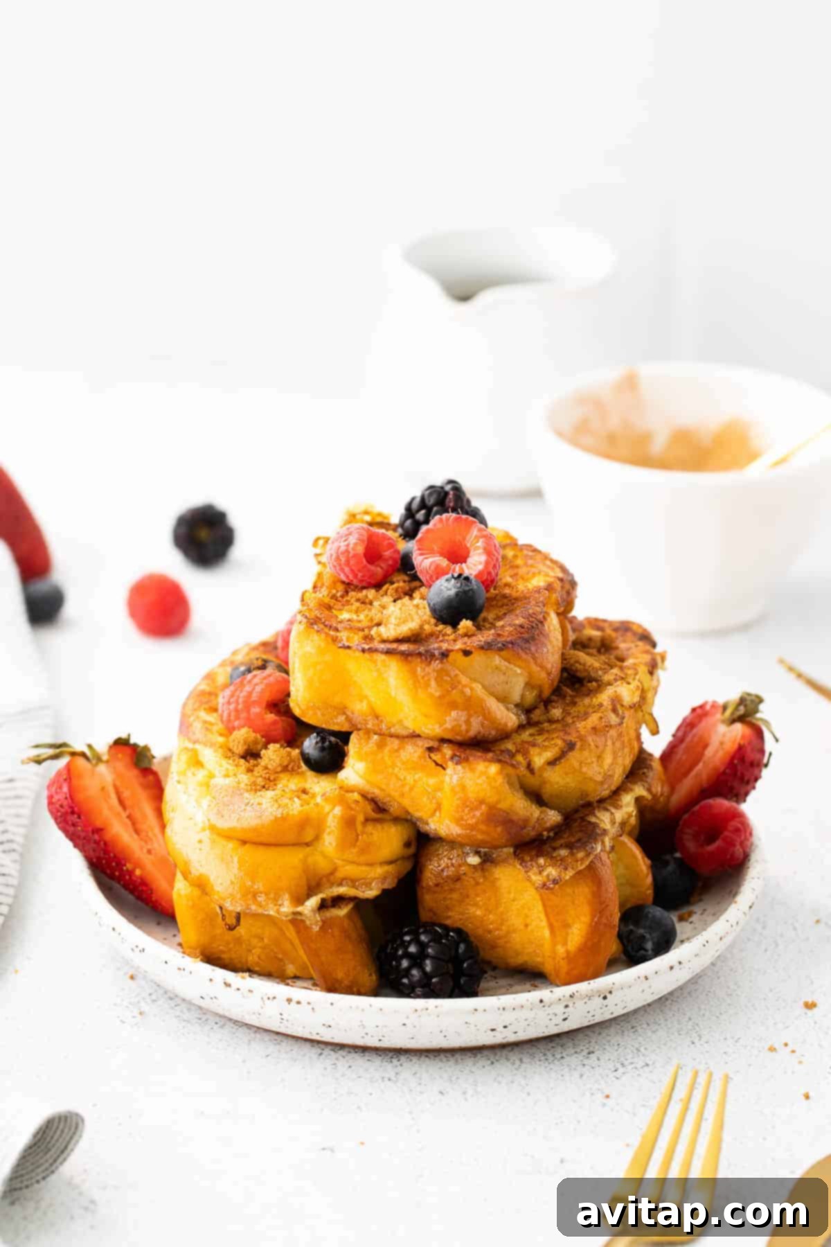 Platter of golden French toast slices generously topped with an array of fresh, colorful berries.