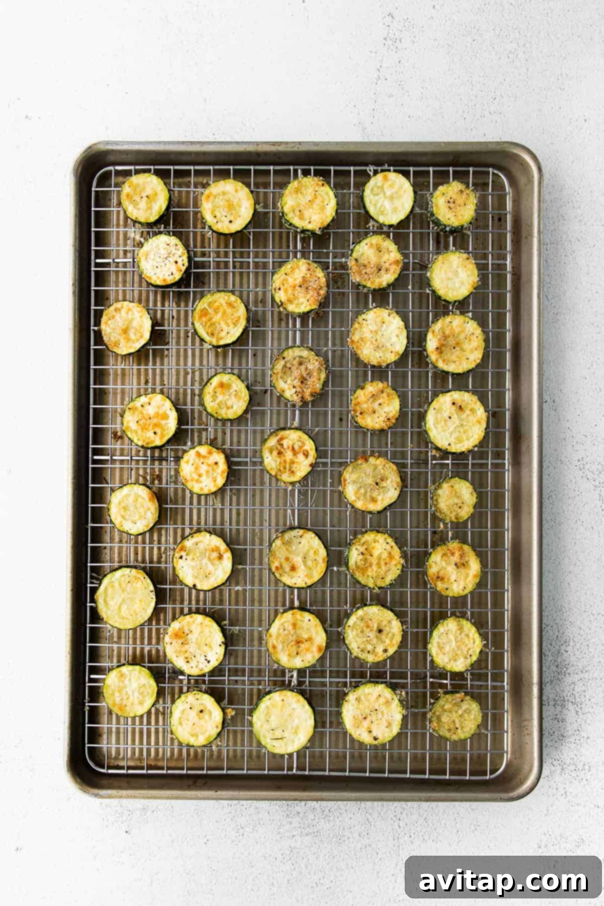 Golden Parmesan Zucchini 4 Crispy Parmesan Baked Zucchini coins arranged neatly on a baking sheet with a cooling rack, freshly out of the oven, golden brown and ready to serve.