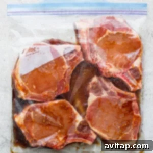 Pork chops immersed in marinade within a plastic bag, ensuring even coating of the meat.