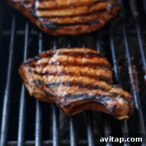 Pork chops cooking on a grill, showing the searing process and early char marks.
