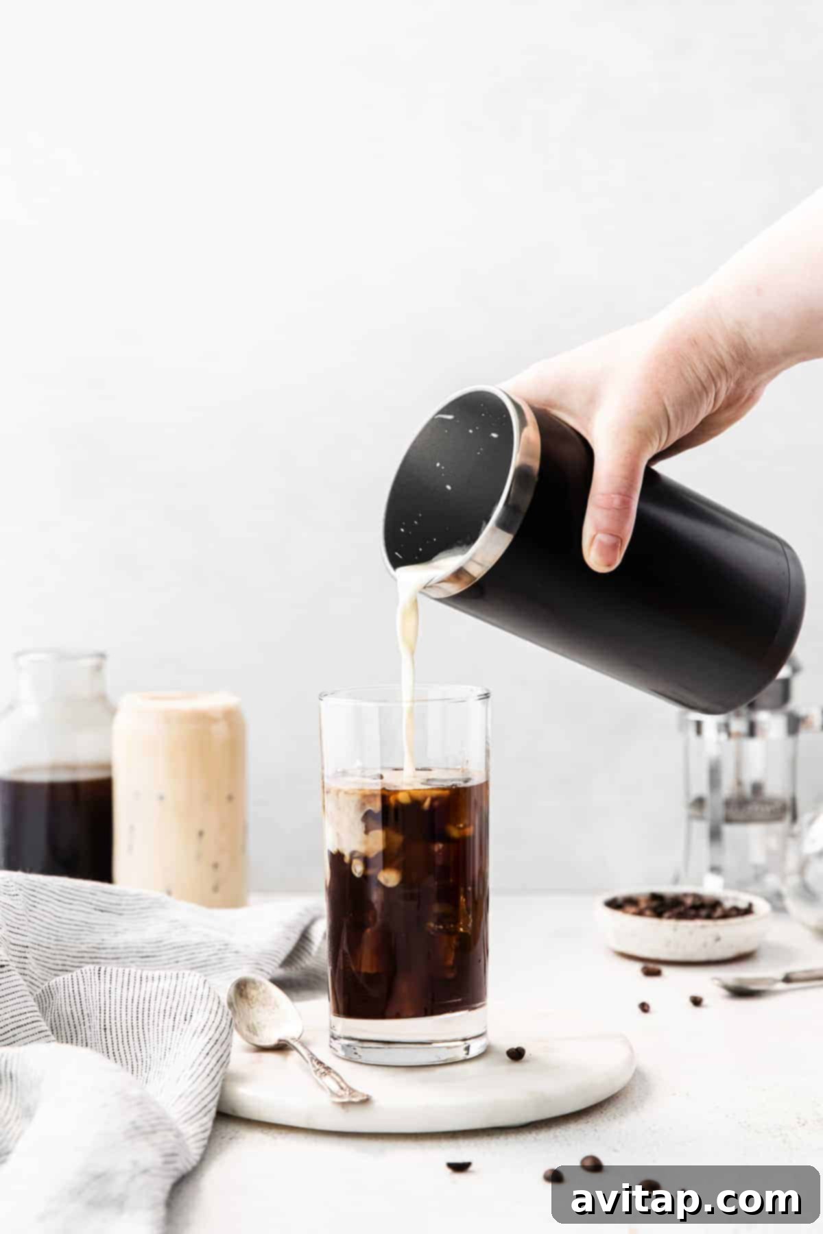 Pouring homemade vanilla sweet cream cold foam into a glass of cold brew coffee.