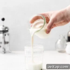 A hand pouring milk into a glass jar with other ingredients.