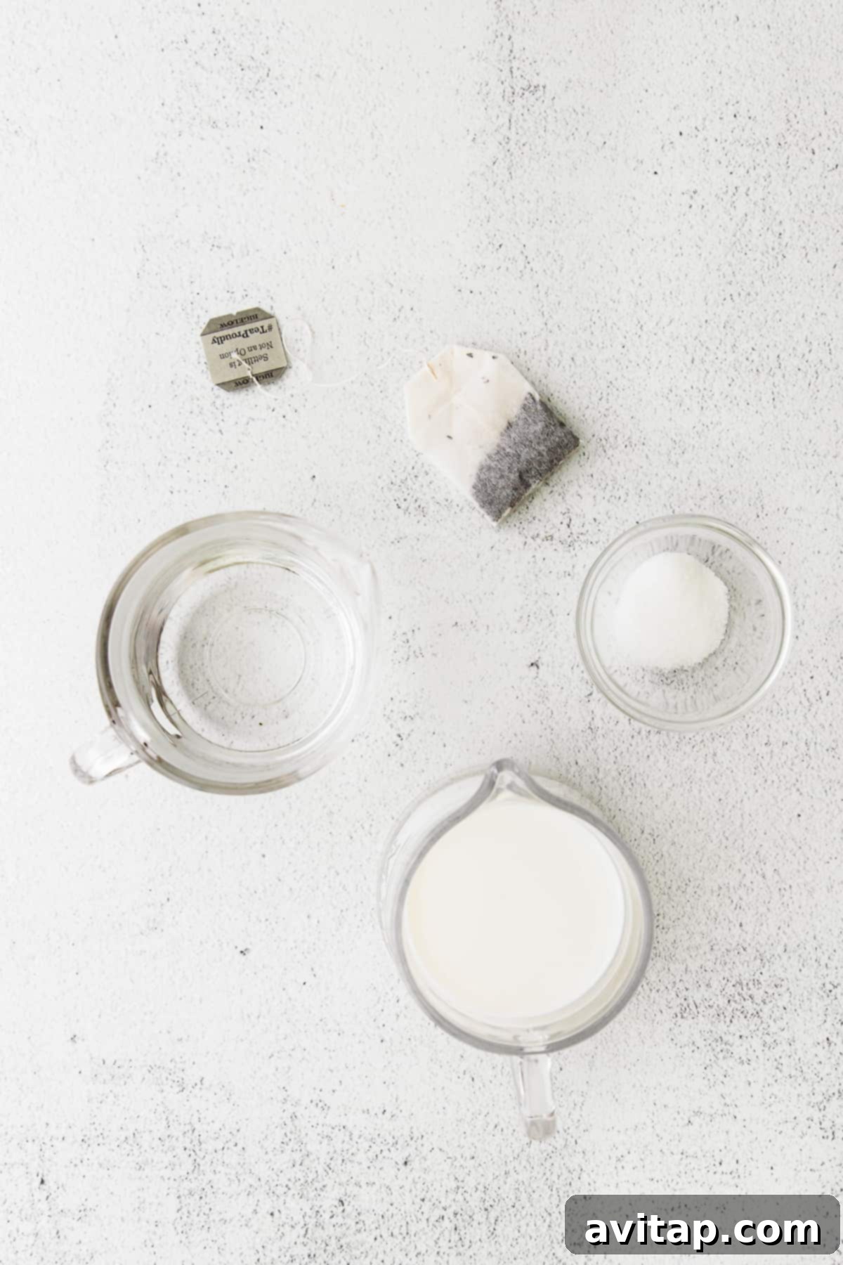 Various ingredients for an Iced London Fog Latte laid out on a kitchen countertop, including tea bags, milk, and sweeteners.