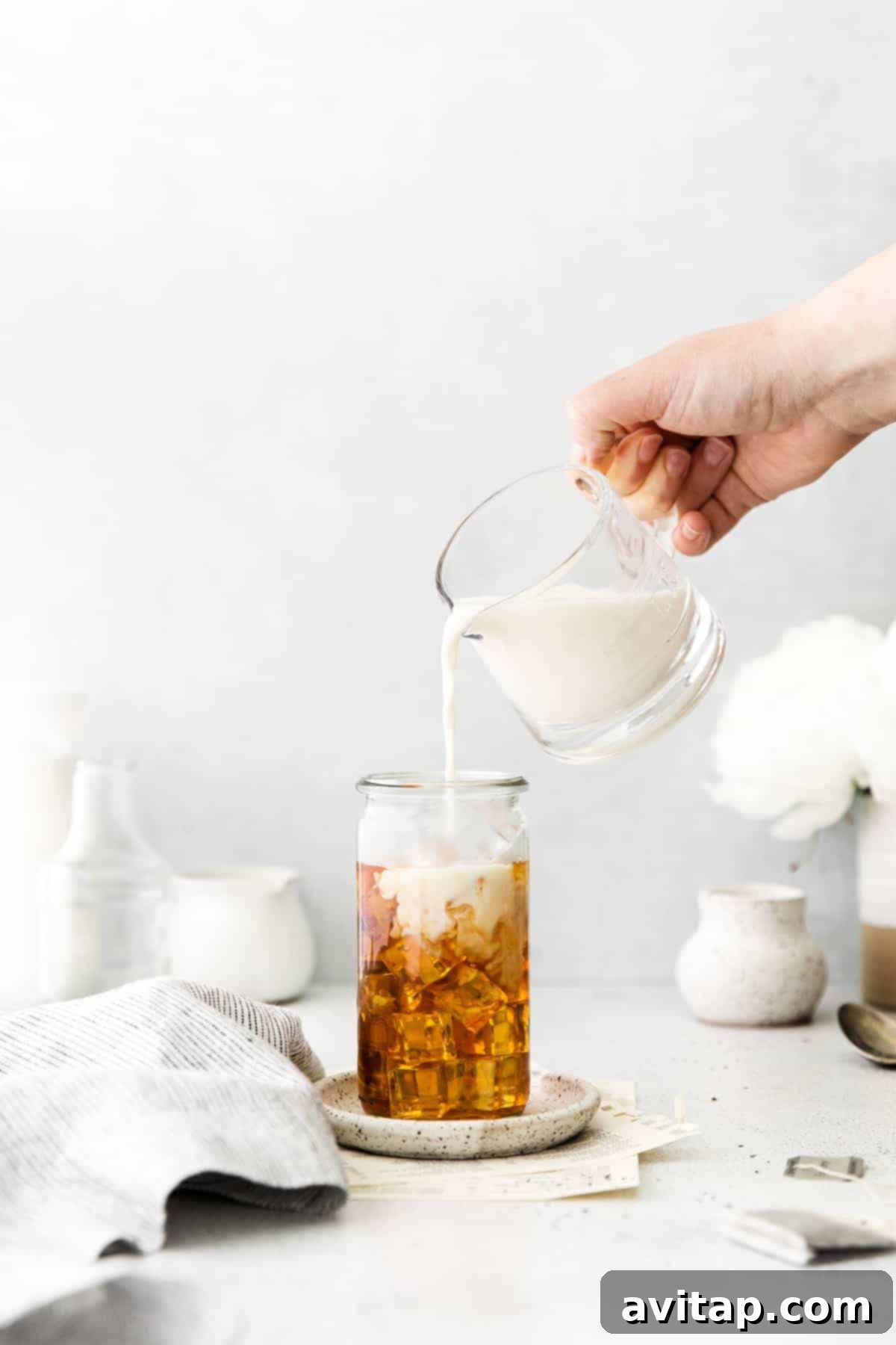 Someone pouring milk over iced Earl Grey tea, creating distinct layers in the glass.