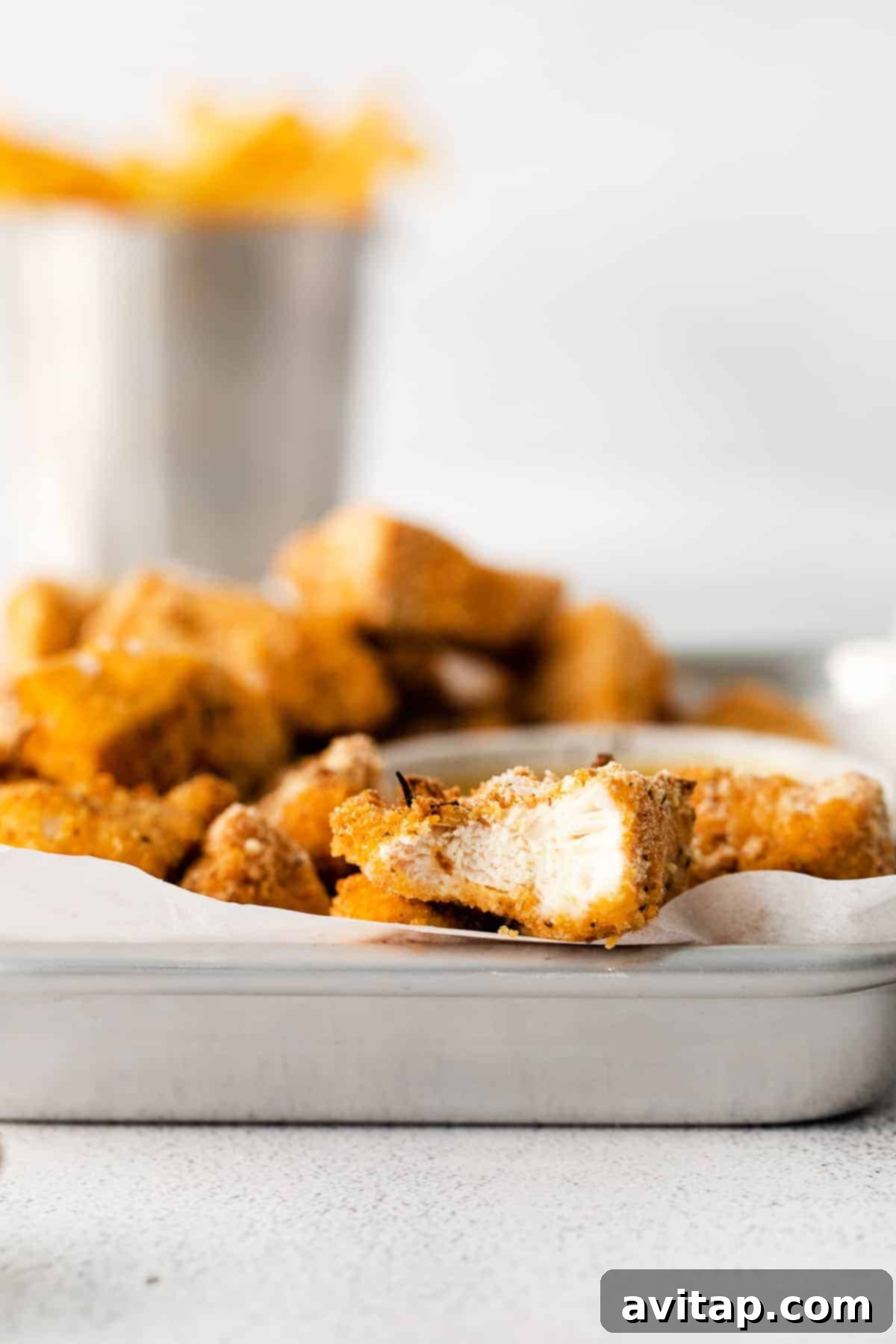 Cooked golden brown chicken nuggets resting in a metal baking sheet after being baked.