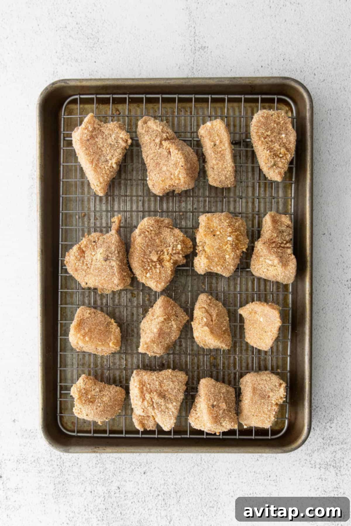 Uncooked breaded chicken nuggets arranged on a baking sheet with a wire rack.