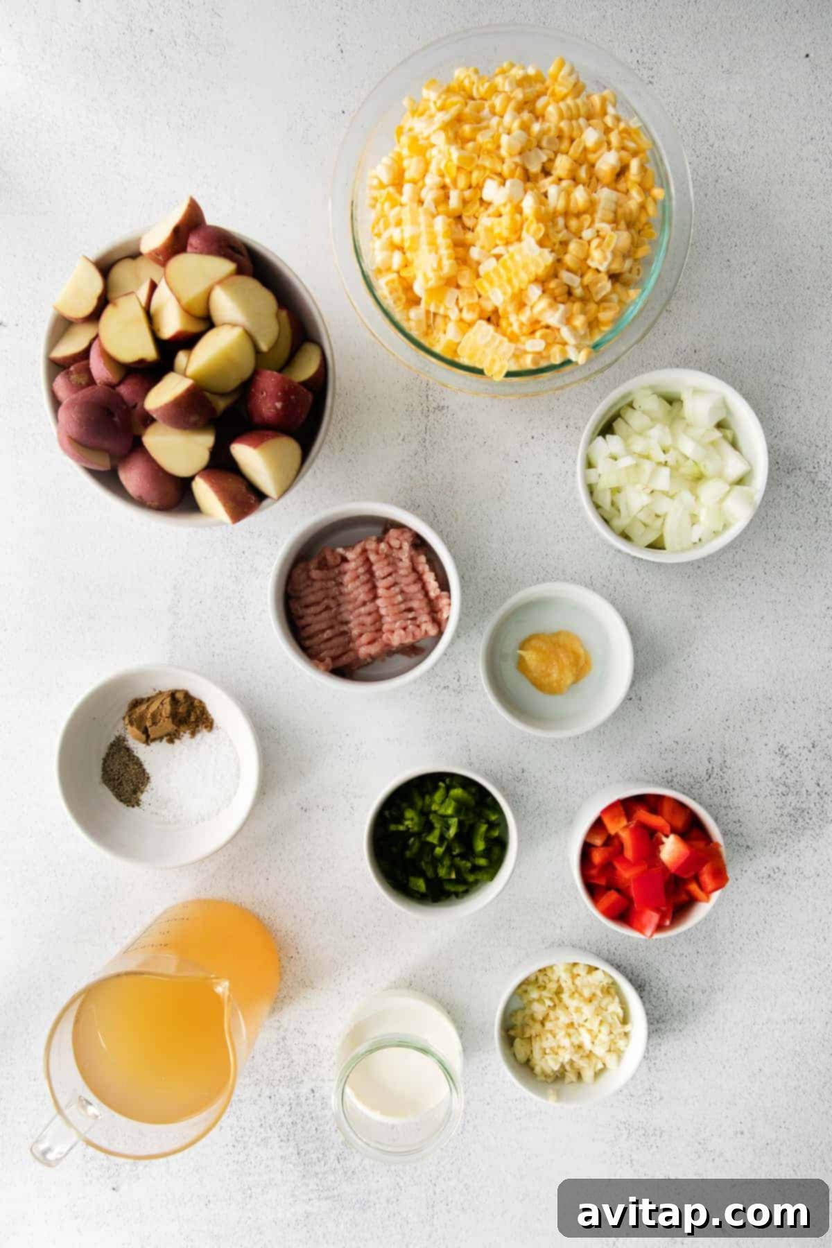 Fresh ingredients for corn chowder laid out on a kitchen counter, including corn cobs, potatoes, onion, garlic, and spices.