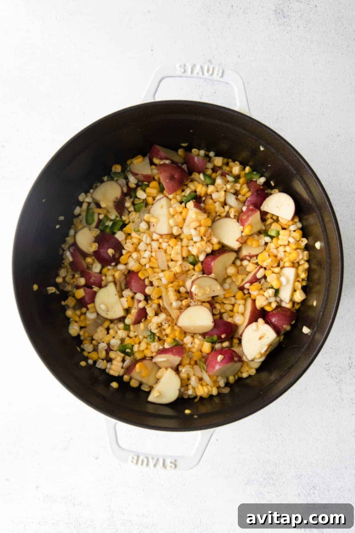 Chopped vegetables and browned pork cooking in a large Dutch oven for corn chowder.