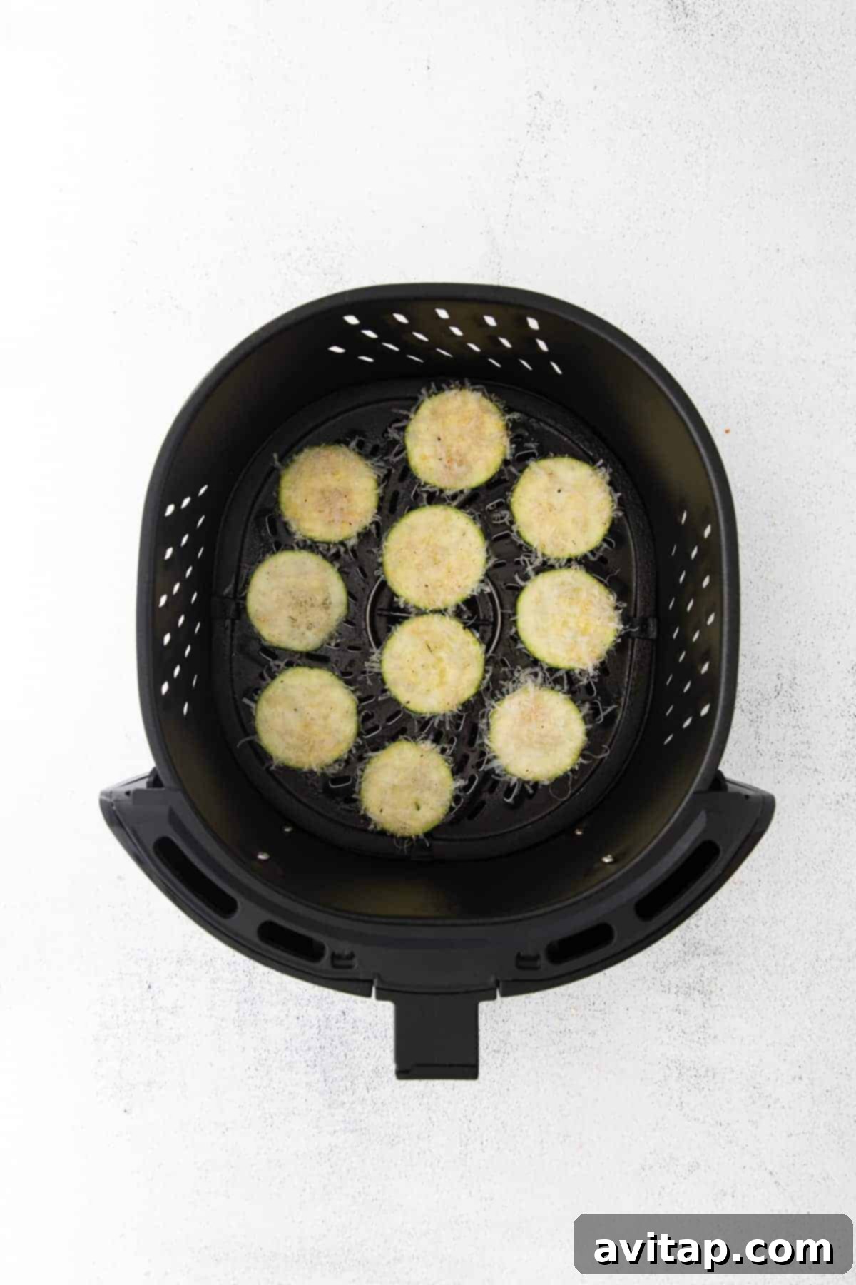 Crispy zucchini slices cooking in an air fryer basket, showing a golden brown crust.