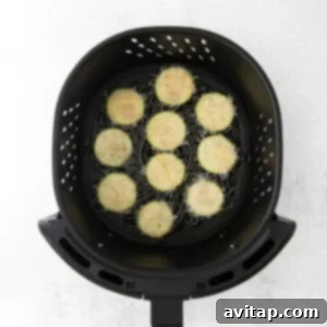 Cooking zucchini coins arranged in a single layer in the air fryer basket.