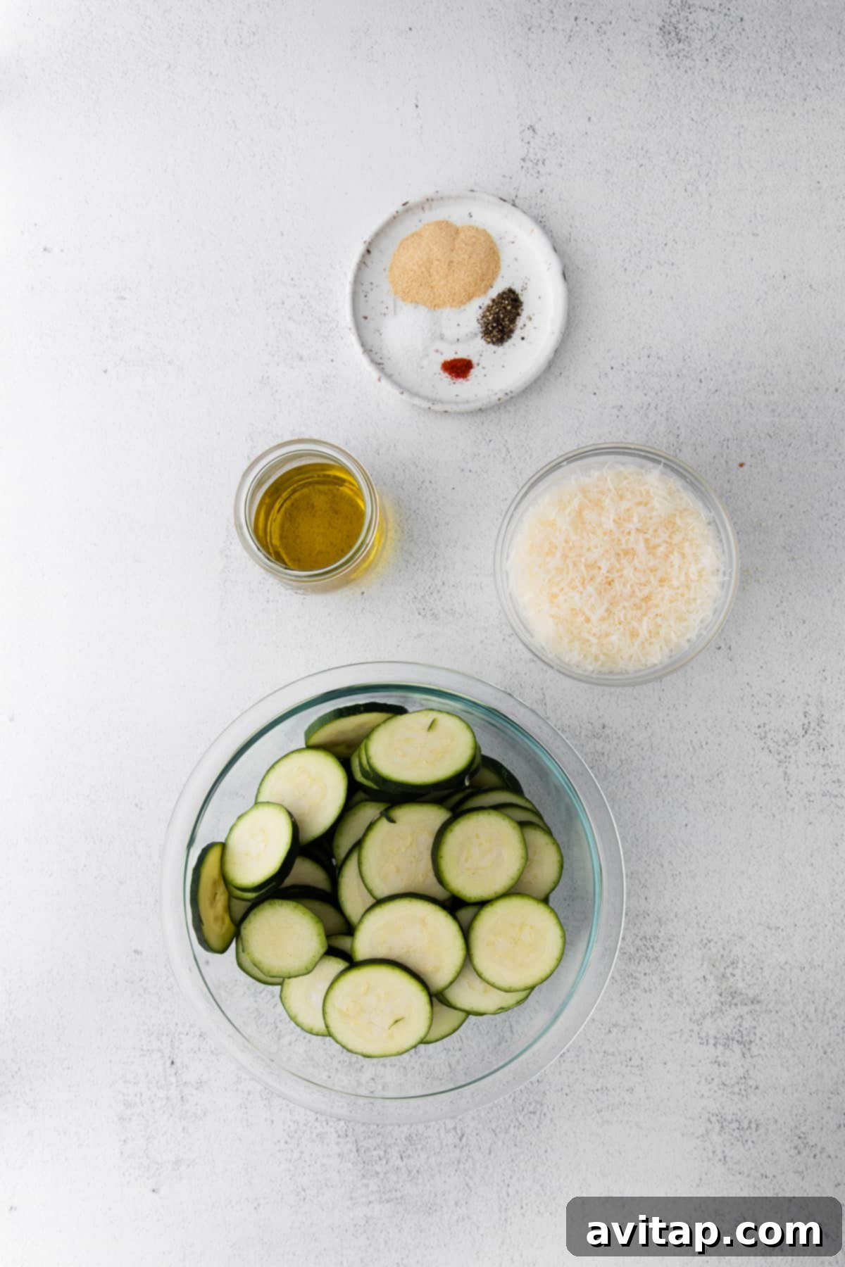 Fresh ingredients laid out for making air fryer zucchini: olive oil, zucchini, parmesan, and spices.