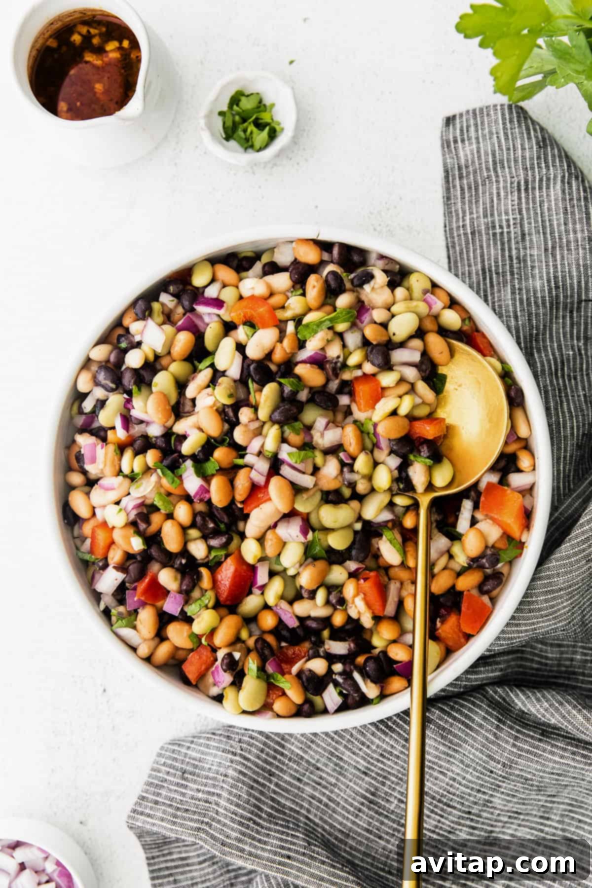 A vibrant, protein-packed bean salad in a rustic bowl, garnished with fresh herbs and a small bowl of zesty dressing on the side. Ideal for a healthy meal.