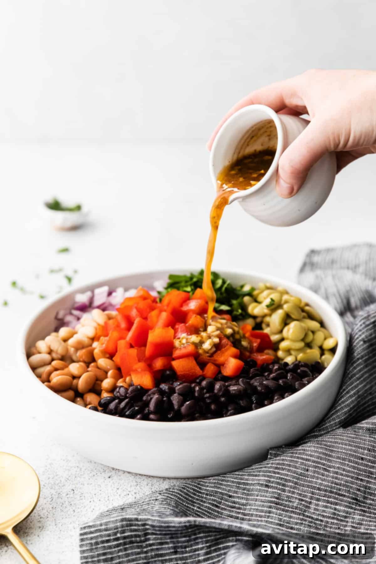 A close-up shot of a zesty dressing being poured over the colorful ingredients of a freshly made bean salad in a large bowl, ready to be tossed and served.
