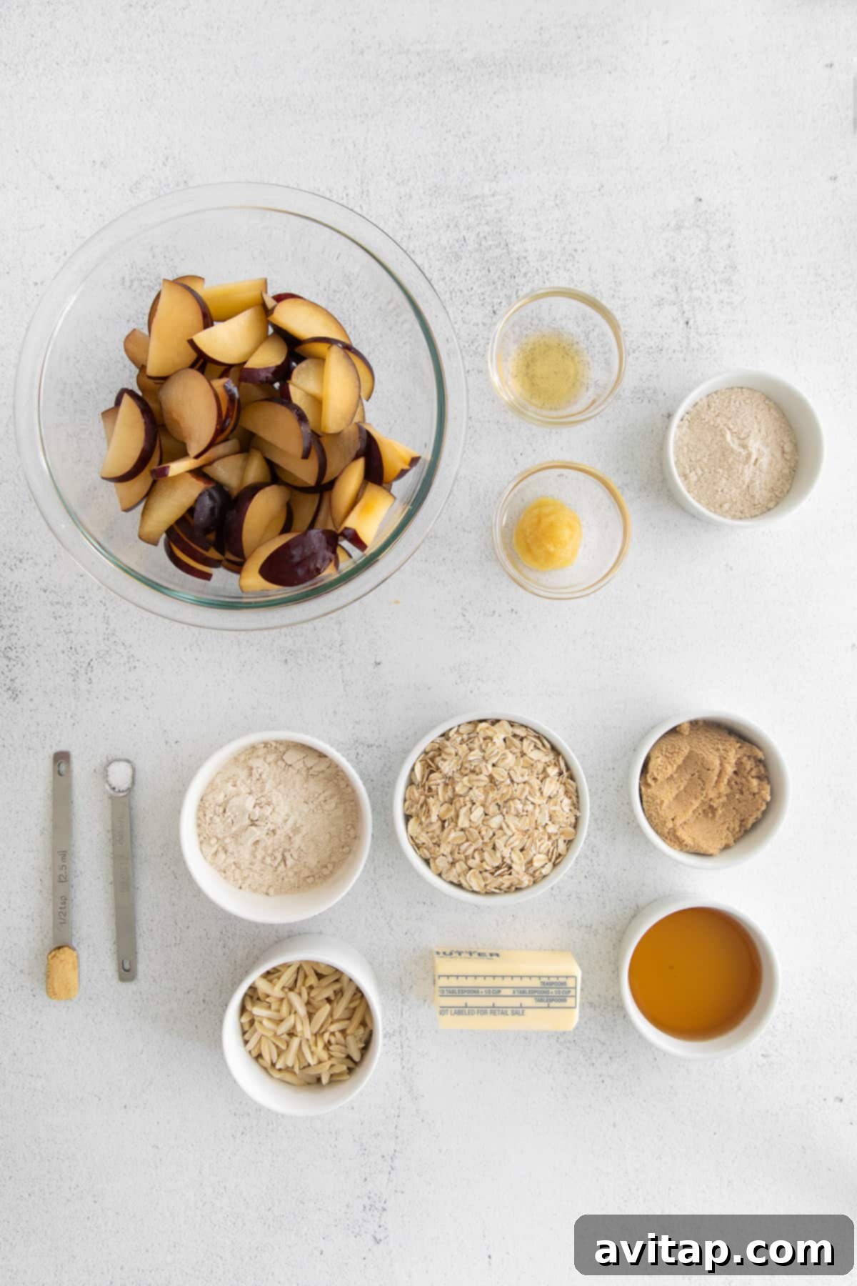 Array of fresh ingredients laid out on a countertop, including plums, oats, flour, and spices, ready for plum crisp preparation.