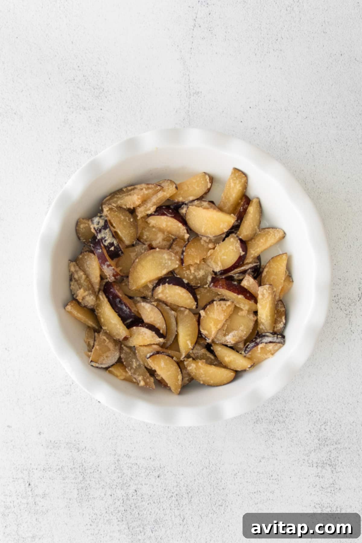 Slices of fresh plums neatly arranged inside a baking dish, forming the base of the crisp.