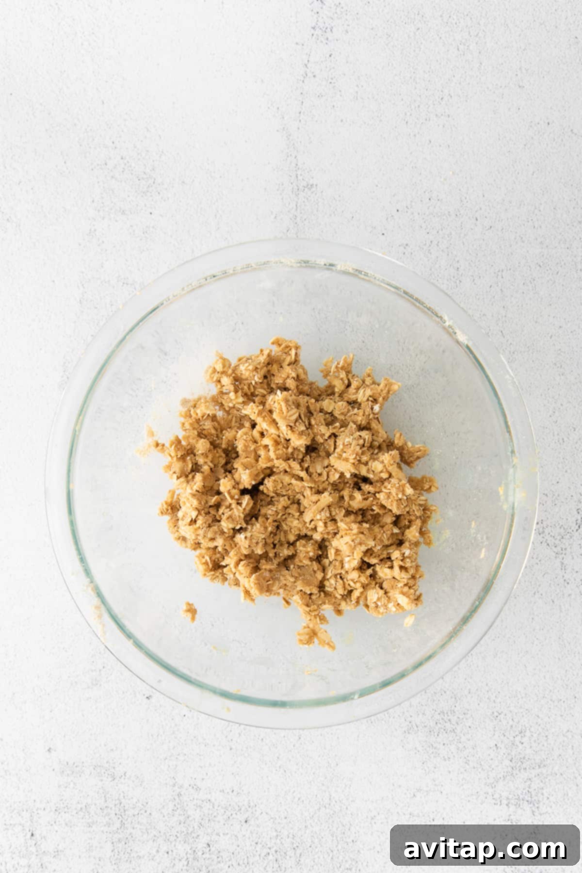 Close-up of the crisp topping mixture before being spread over the plums, showing oats, nuts, and butter crumbles.