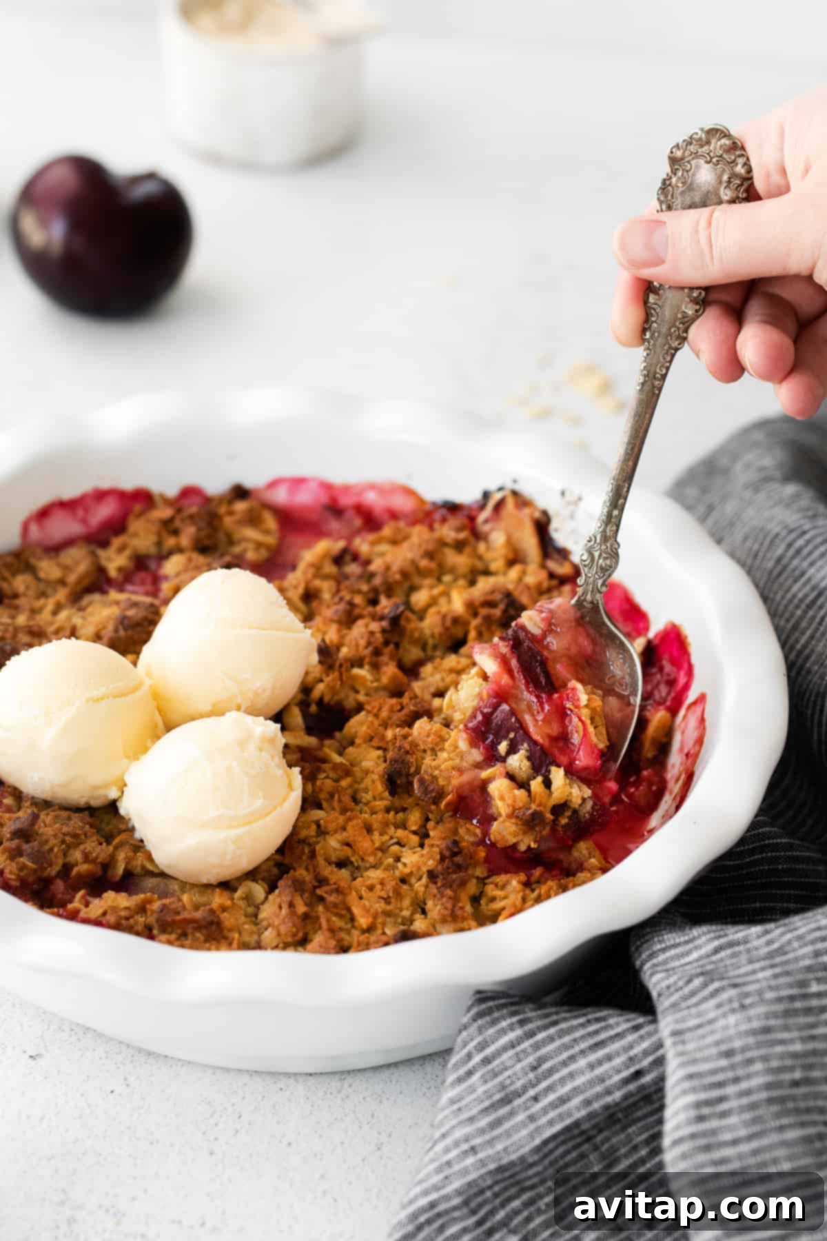 A spoon scooping a generous portion of warm plum crisp from the baking dish.