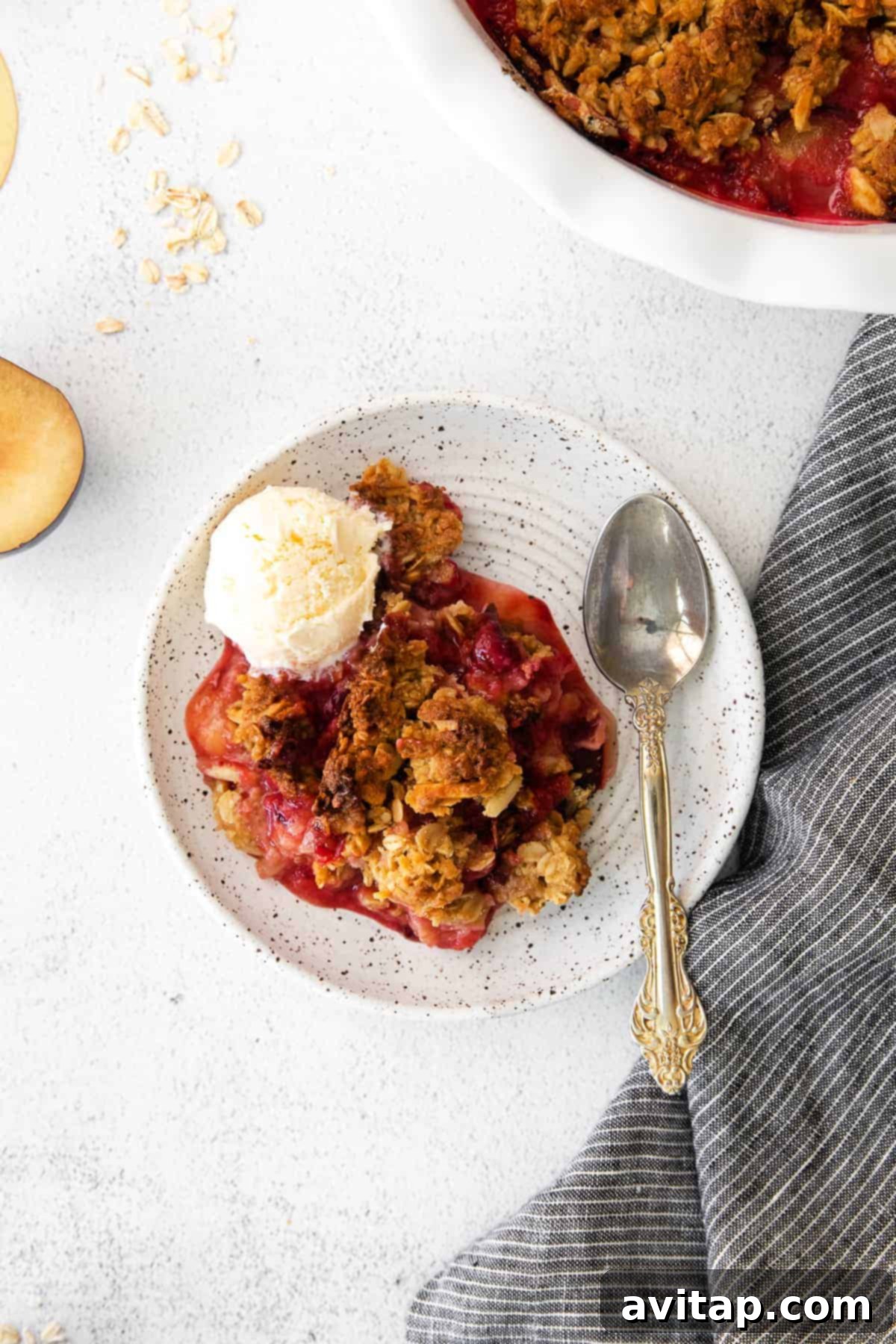 A single serving of plum crisp on a white plate, with a spoon nearby, inviting a bite.