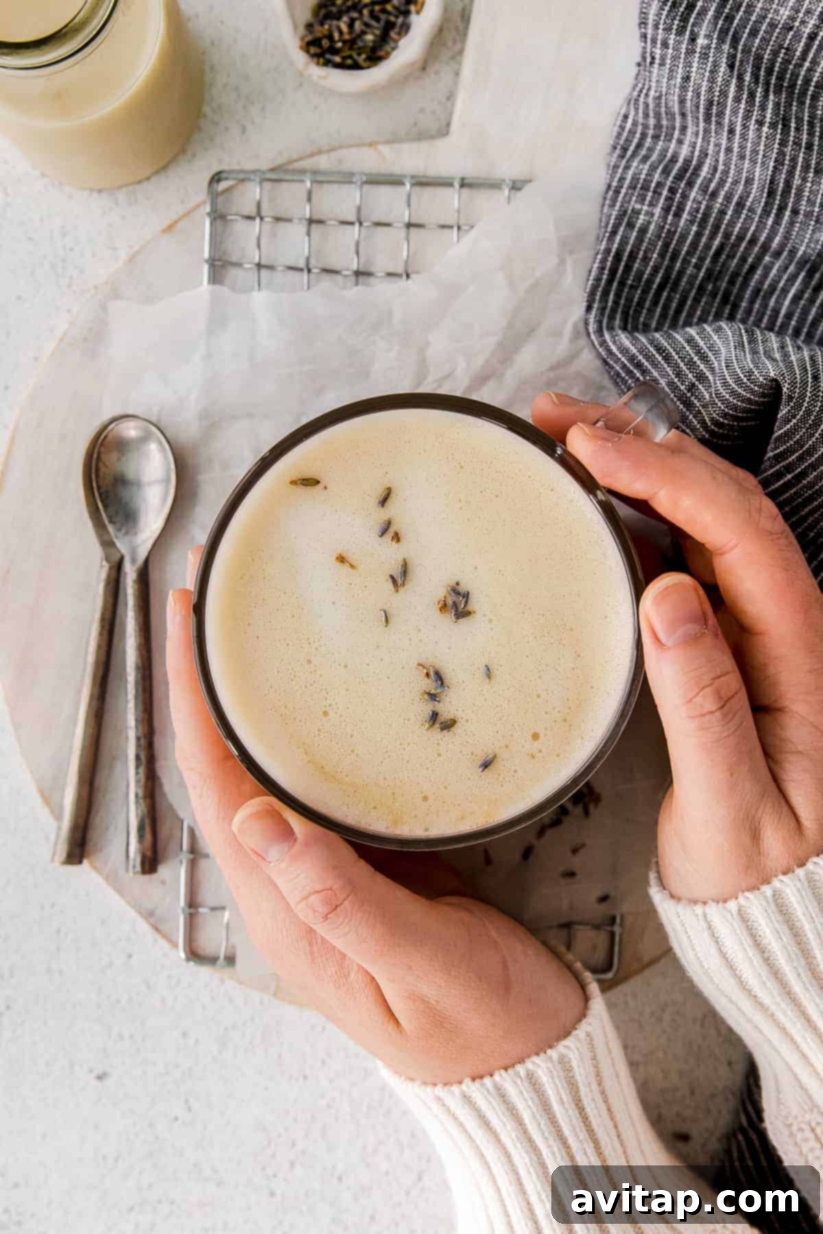 Start your day with this deliciously easy London fog drink! This latte is made with earl grey tea, your favorite steamed milk and slightly sweetened. A person warmly holding a mug of London fog drink, emphasizing comfort and coziness.