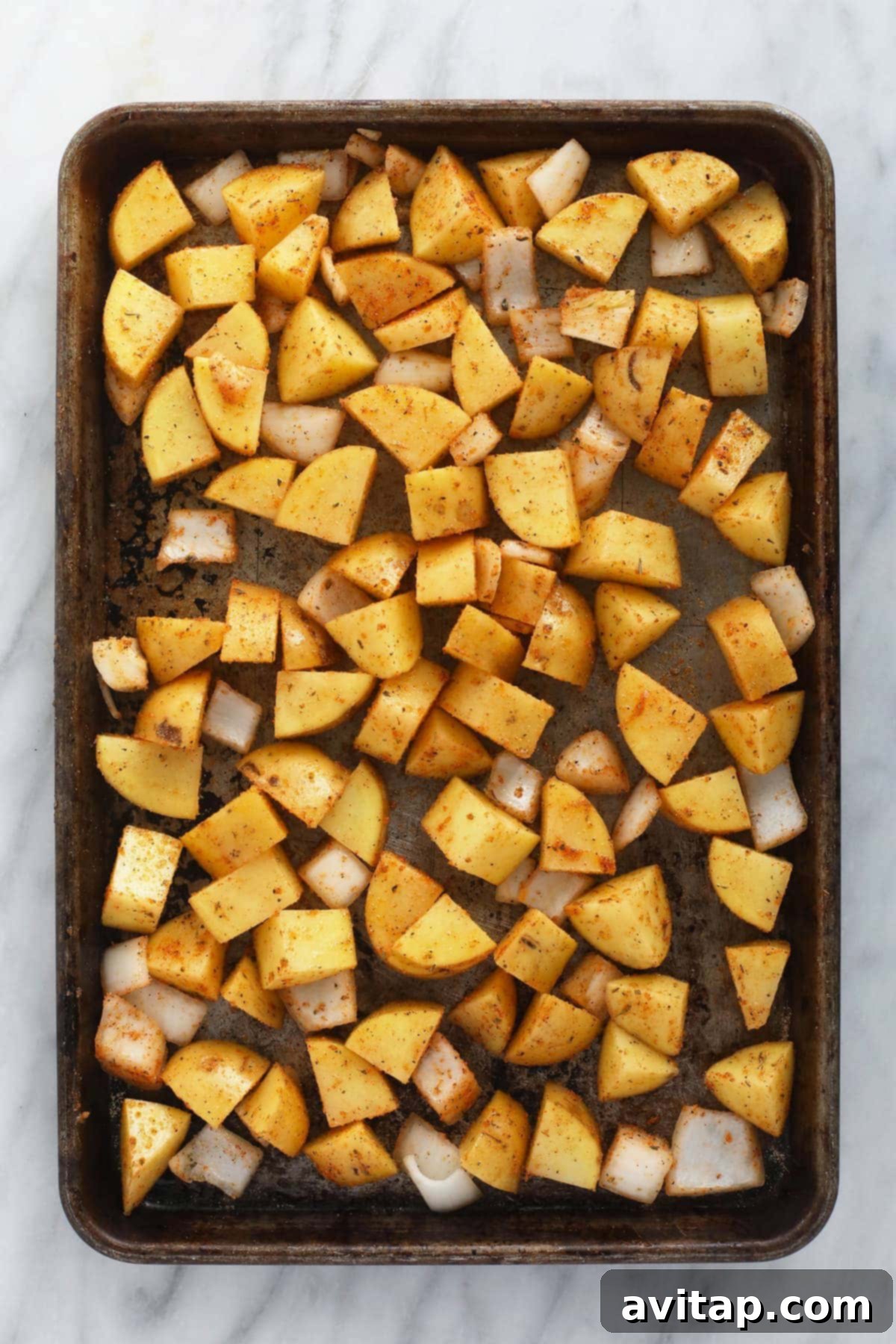 Sliced breakfast potatoes, red bell pepper, and onion on a baking sheet, ready for the oven