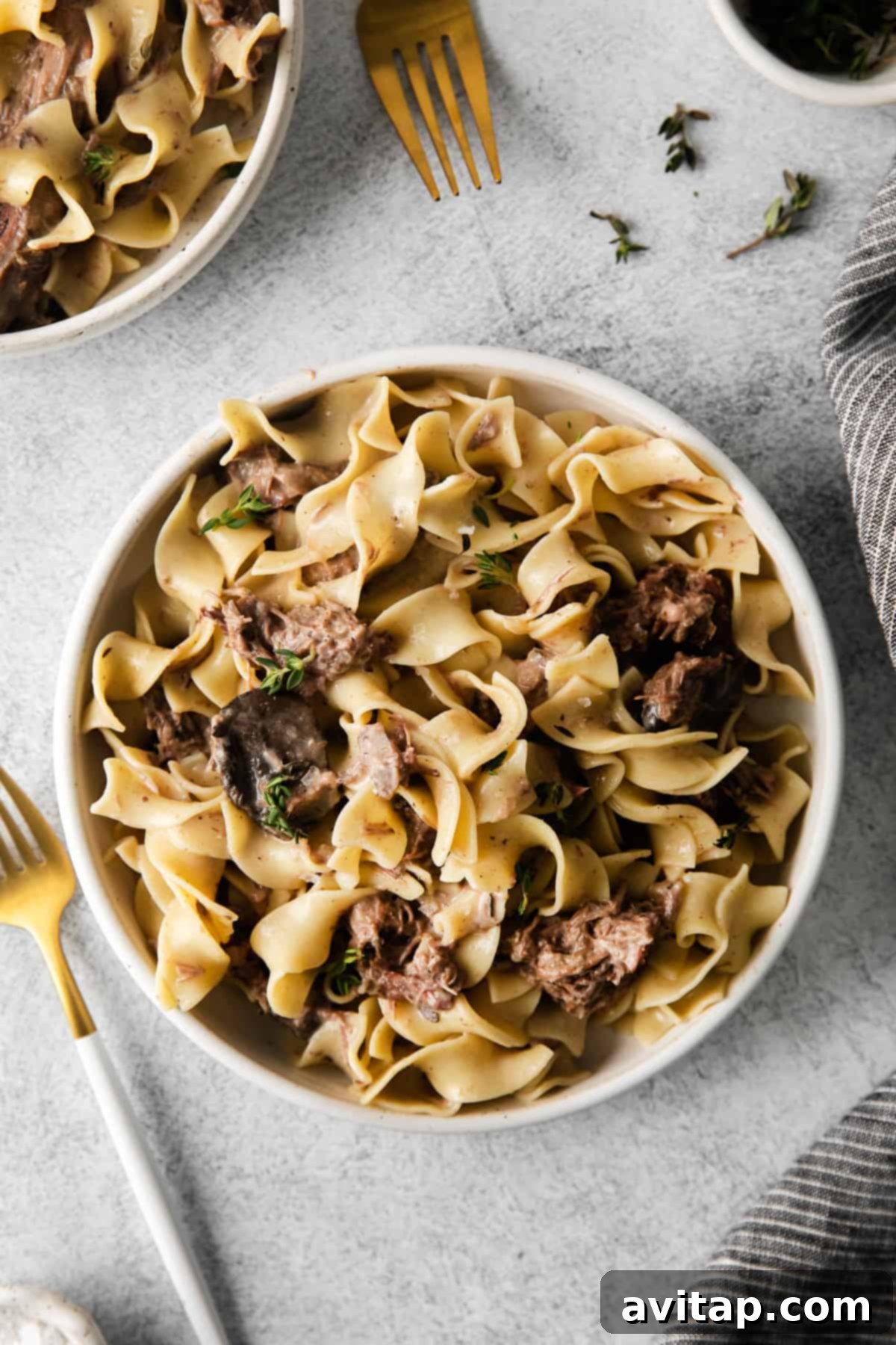 Bowl of Slow Cooker Beef Stroganoff with egg noodles, garnished with fresh parsley