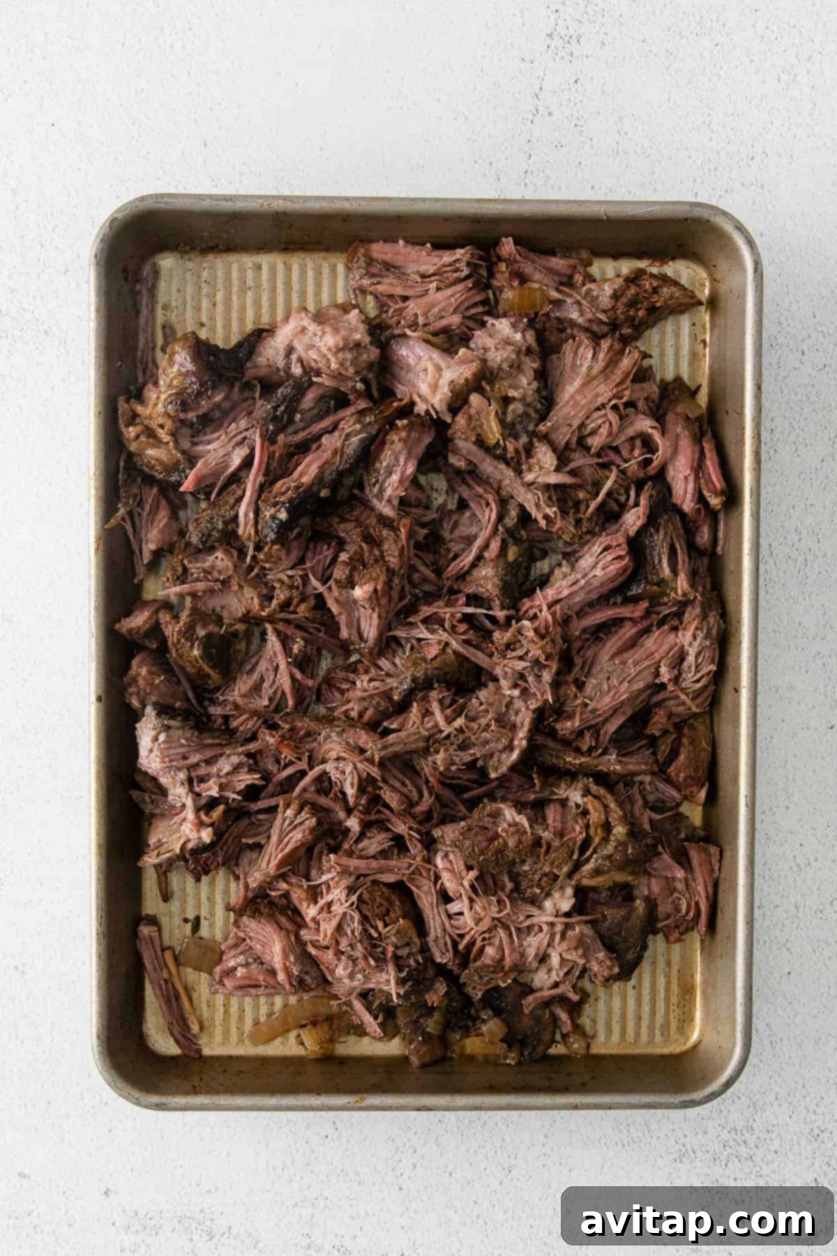 Shredded beef resting on a baking sheet after slow cooking