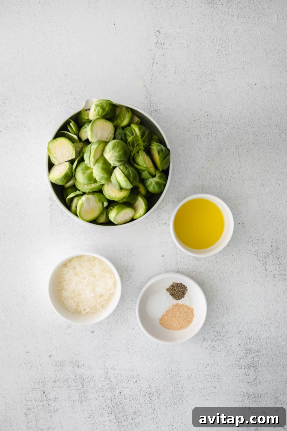 Ingredients for air fryer Brussels sprouts laid out on a kitchen counter: fresh Brussels sprouts, olive oil, garlic powder, Parmesan cheese, salt, and pepper.