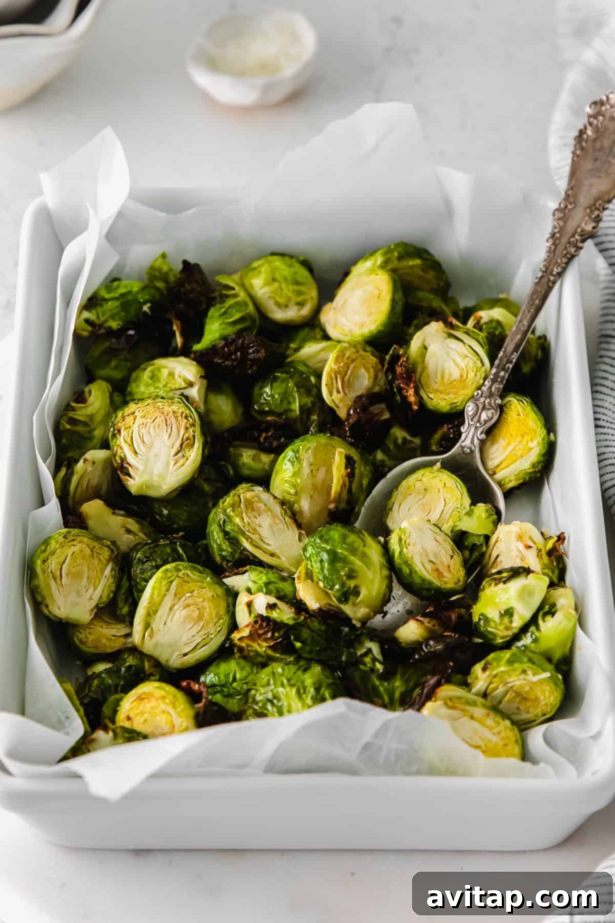 A serving of air fryer Brussels sprouts presented in a white casserole dish, garnished with fresh herbs.