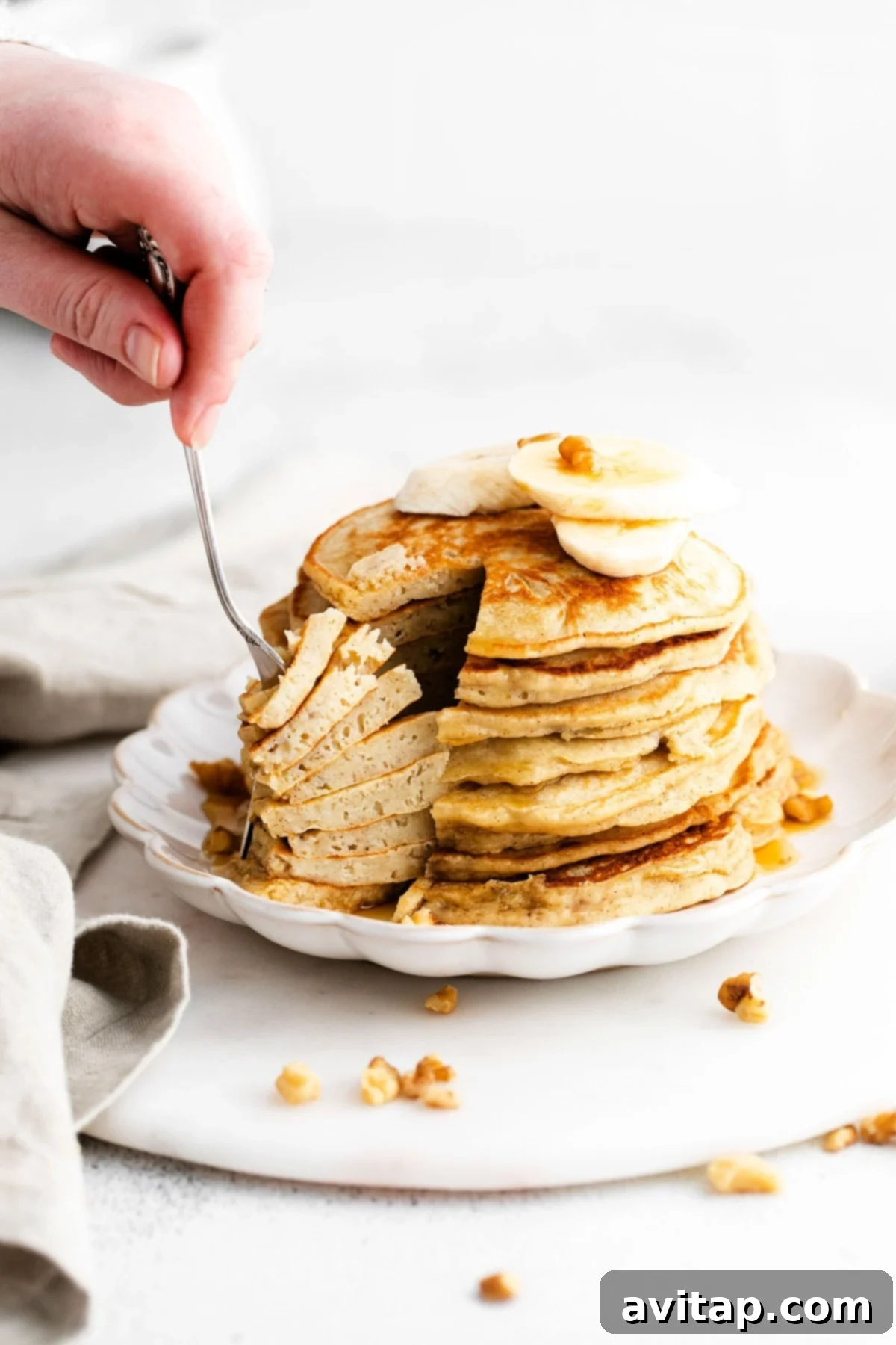 Enjoying a Stack of Banana Pancakes A fork digging into a stack of healthy banana pancakes, showing the fluffy interior and golden-brown exterior, with maple syrup cascading down