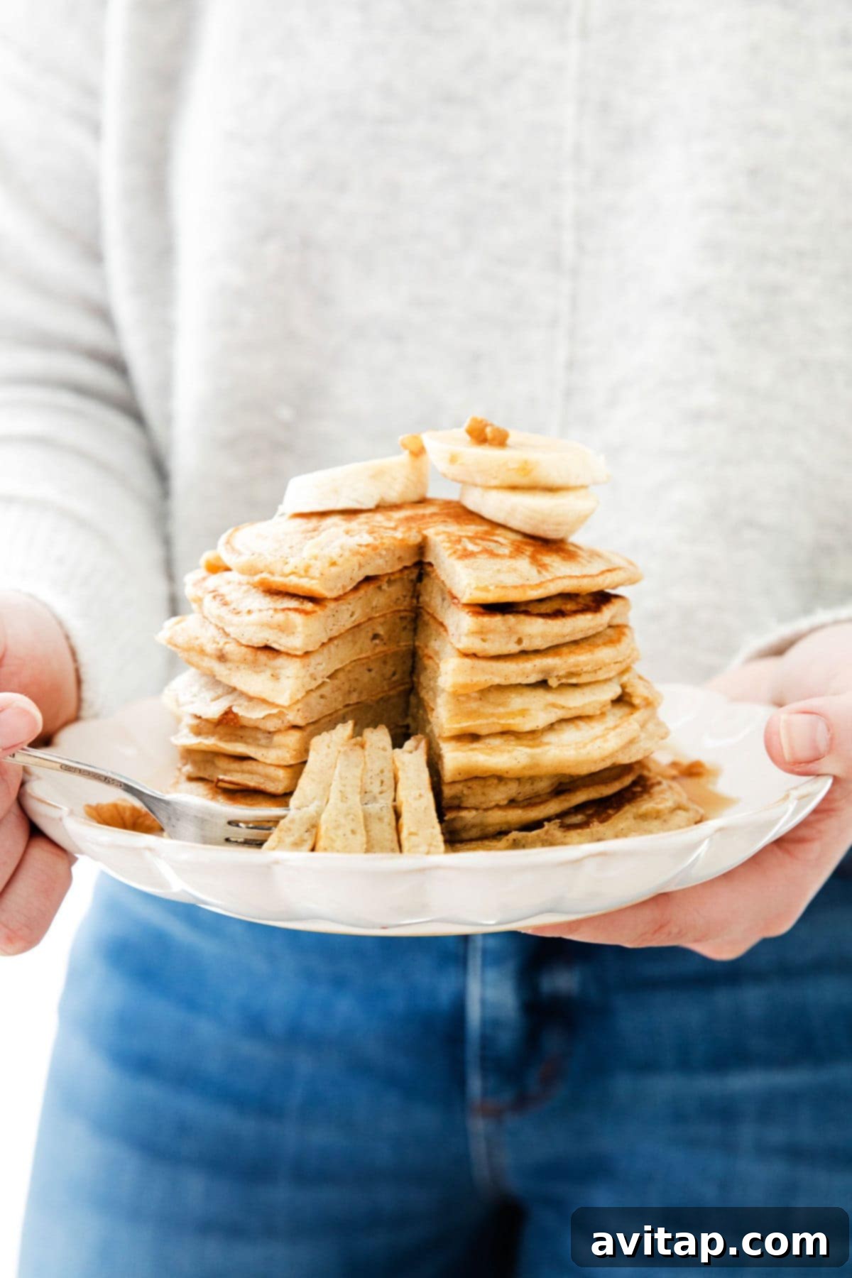 Enjoying a Plate of Easy and Healthy Banana Pancakes A person holding a plate with a stack of easy banana pancakes, garnished with fresh fruit.