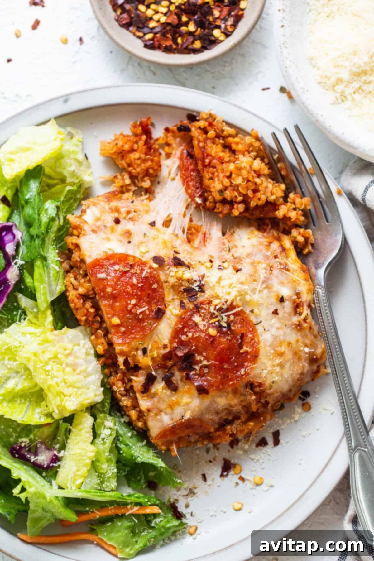 Easy Pizza Quinoa Bake 6 A serving of pepperoni pizza quinoa casserole on a plate, with a side salad.