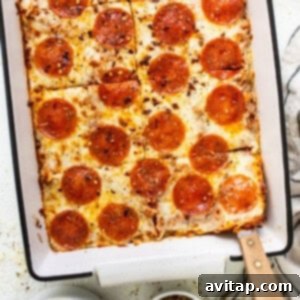 Easy Pizza Quinoa Bake 7 Pepperoni pizza in a baking dish with a spoon, showing a serving.