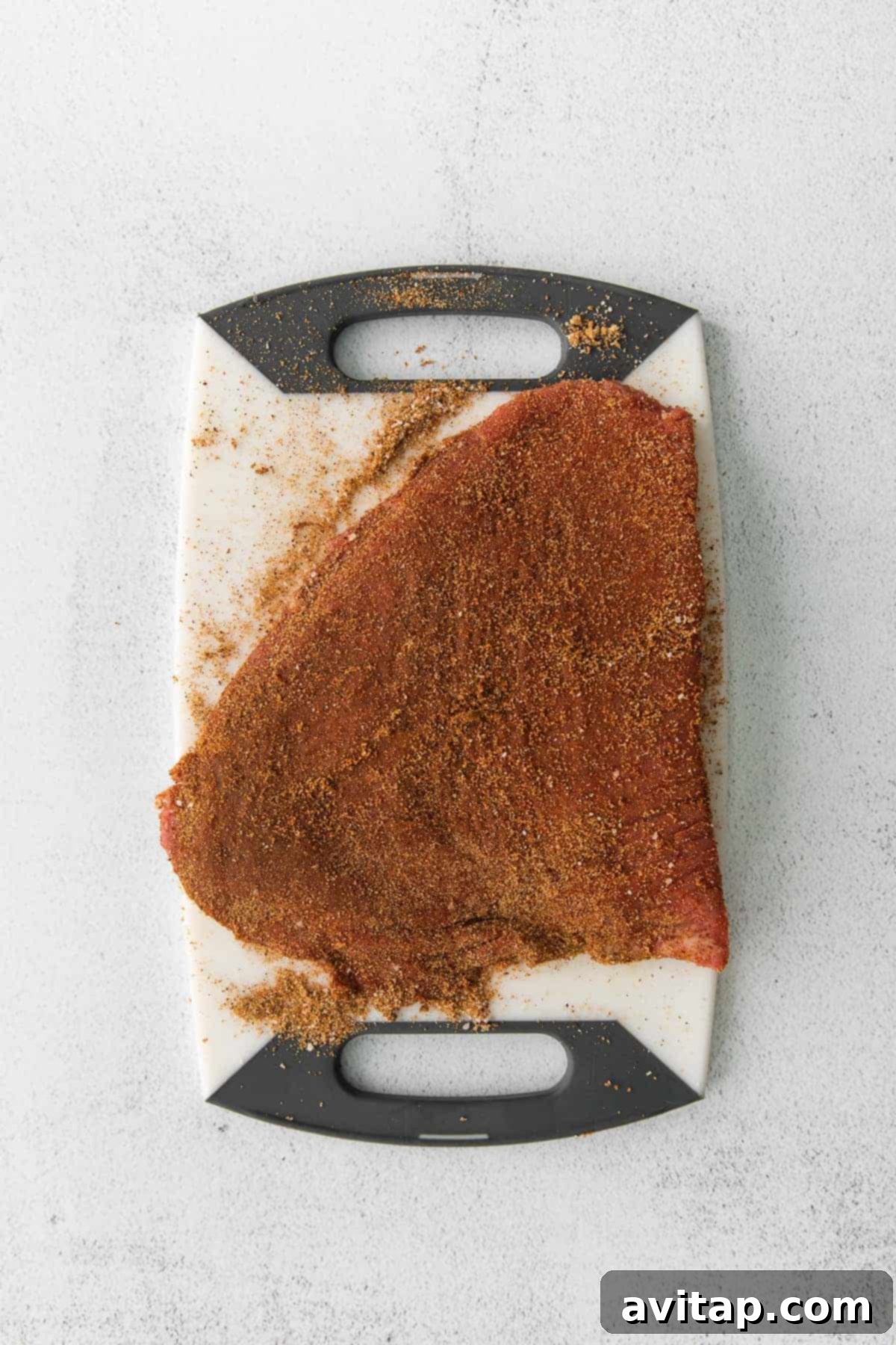 A flank steak generously coated with homemade steak taco seasoning, ready for cooking.