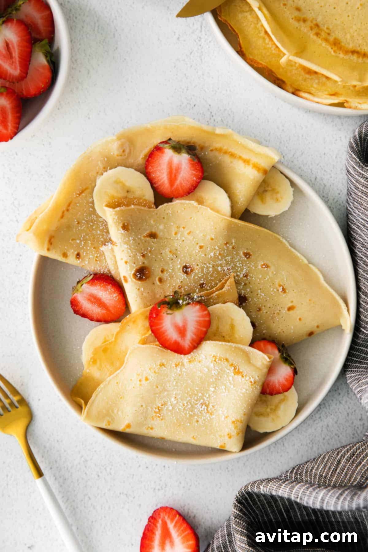 Golden-brown crepes delicately folded on a plate, garnished with fresh strawberries and sliced bananas, ready to be enjoyed.