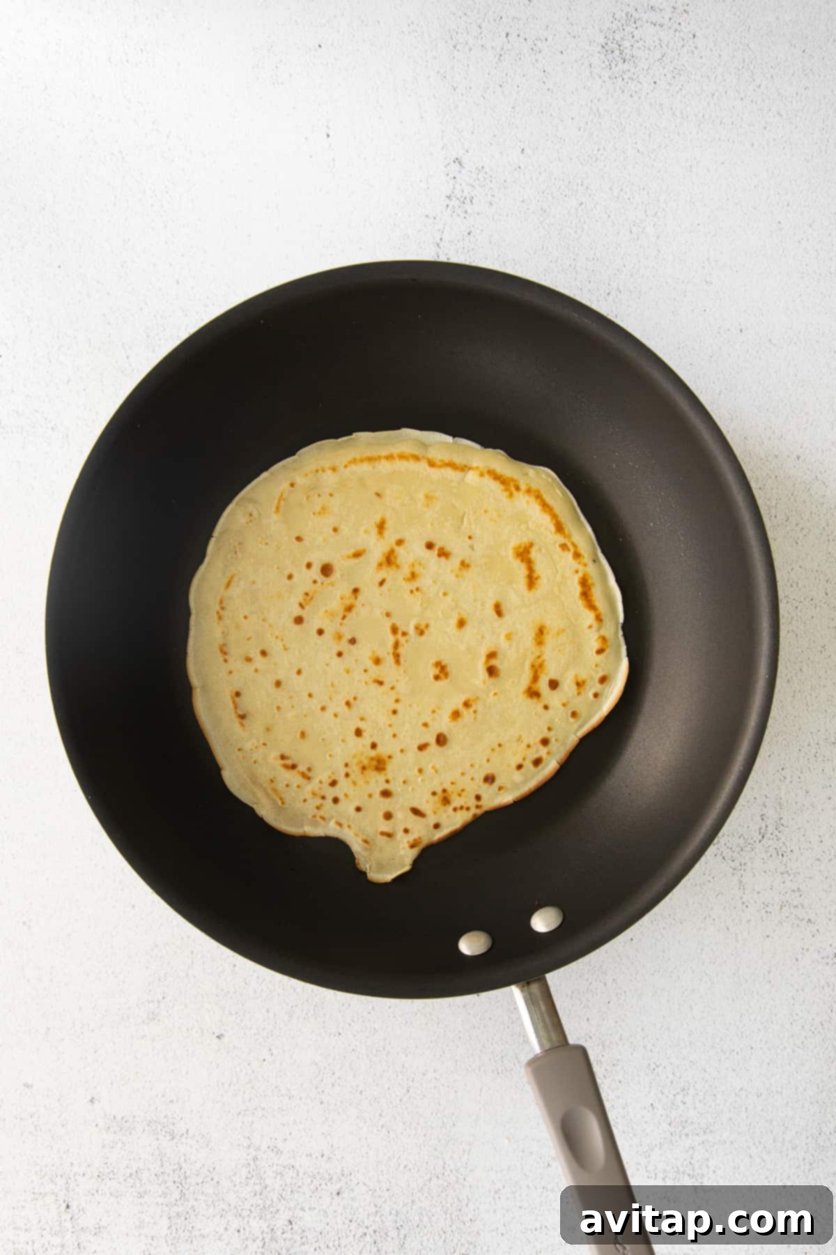 A perfectly cooked golden-brown crepe resting in a nonstick pan, ready to be flipped or served.